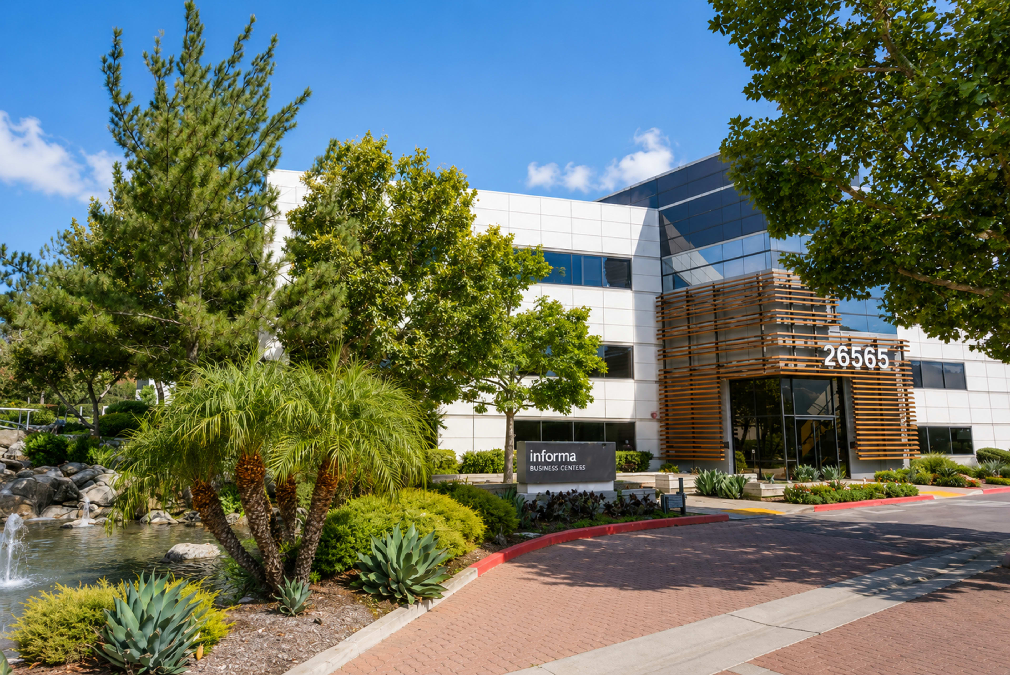 The image shows a modern business center with a water feature and landscaped greenery in front, featuring a sign that reads "inforia" and the address "26565."