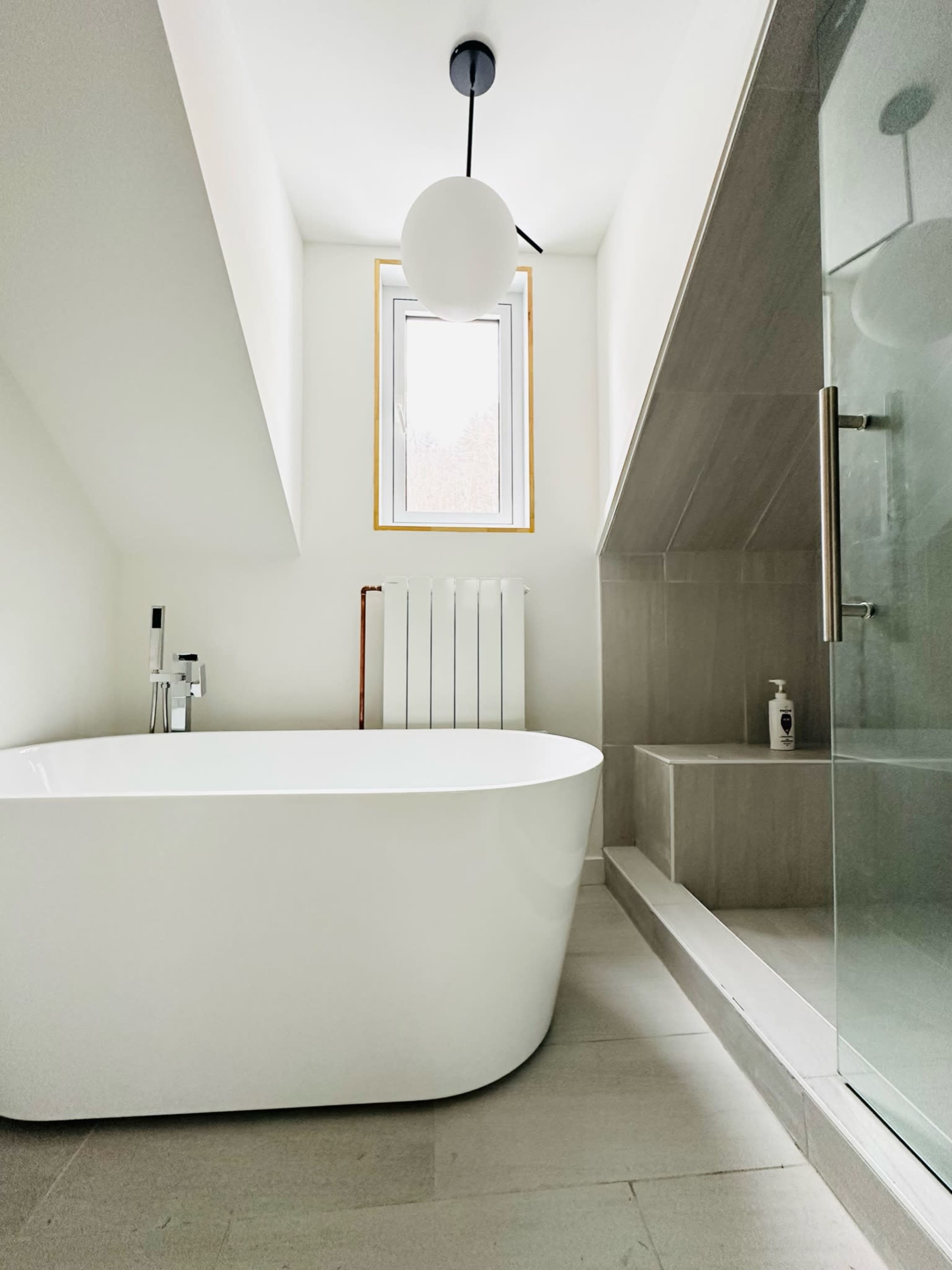 A modern bathroom featuring a freestanding bathtub, a glass shower enclosure, and a window with a minimalist design.