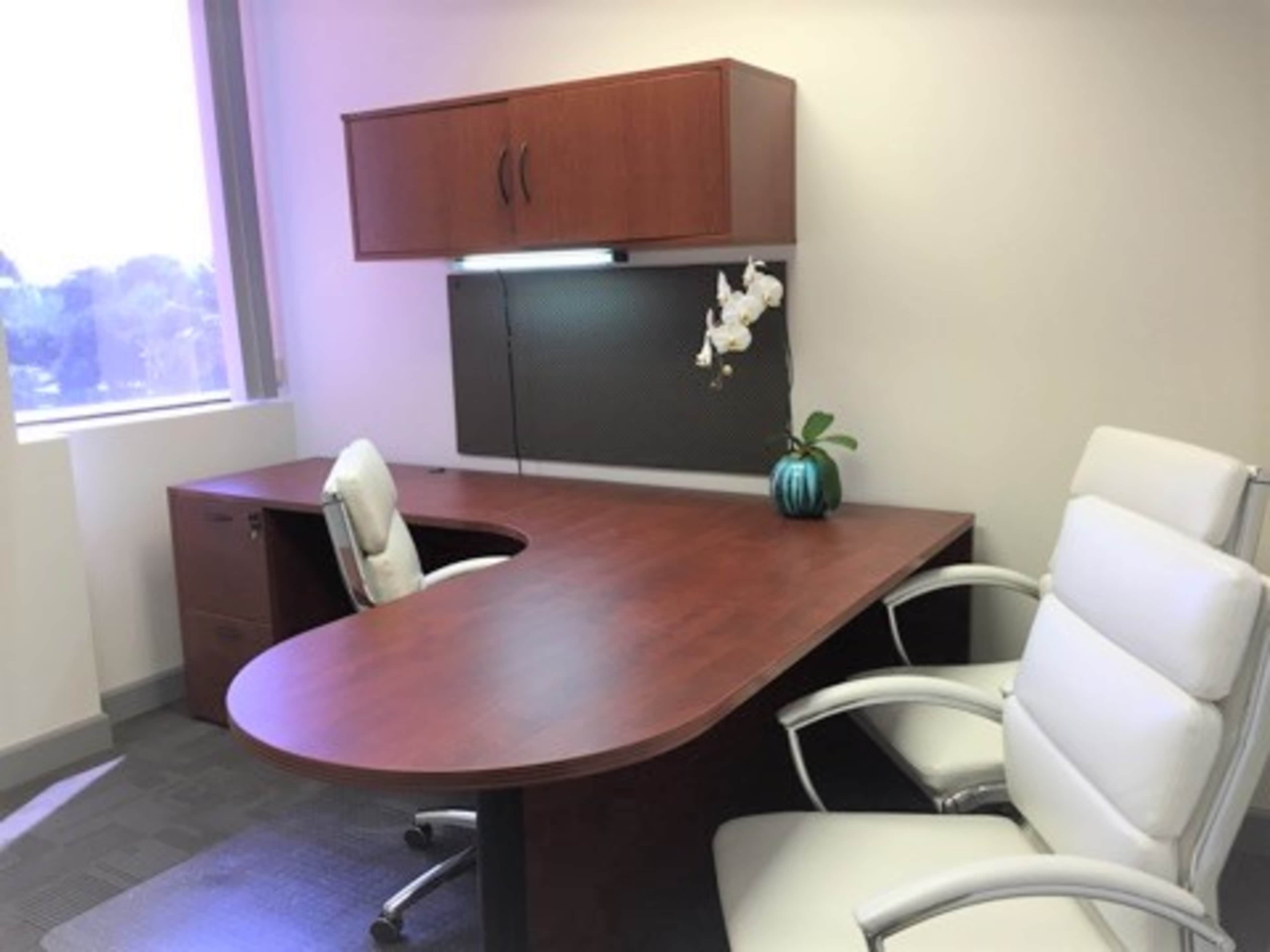 A modern office setup with a round wooden desk, two white chairs, a file cabinet, and a small potted plant on the desk.