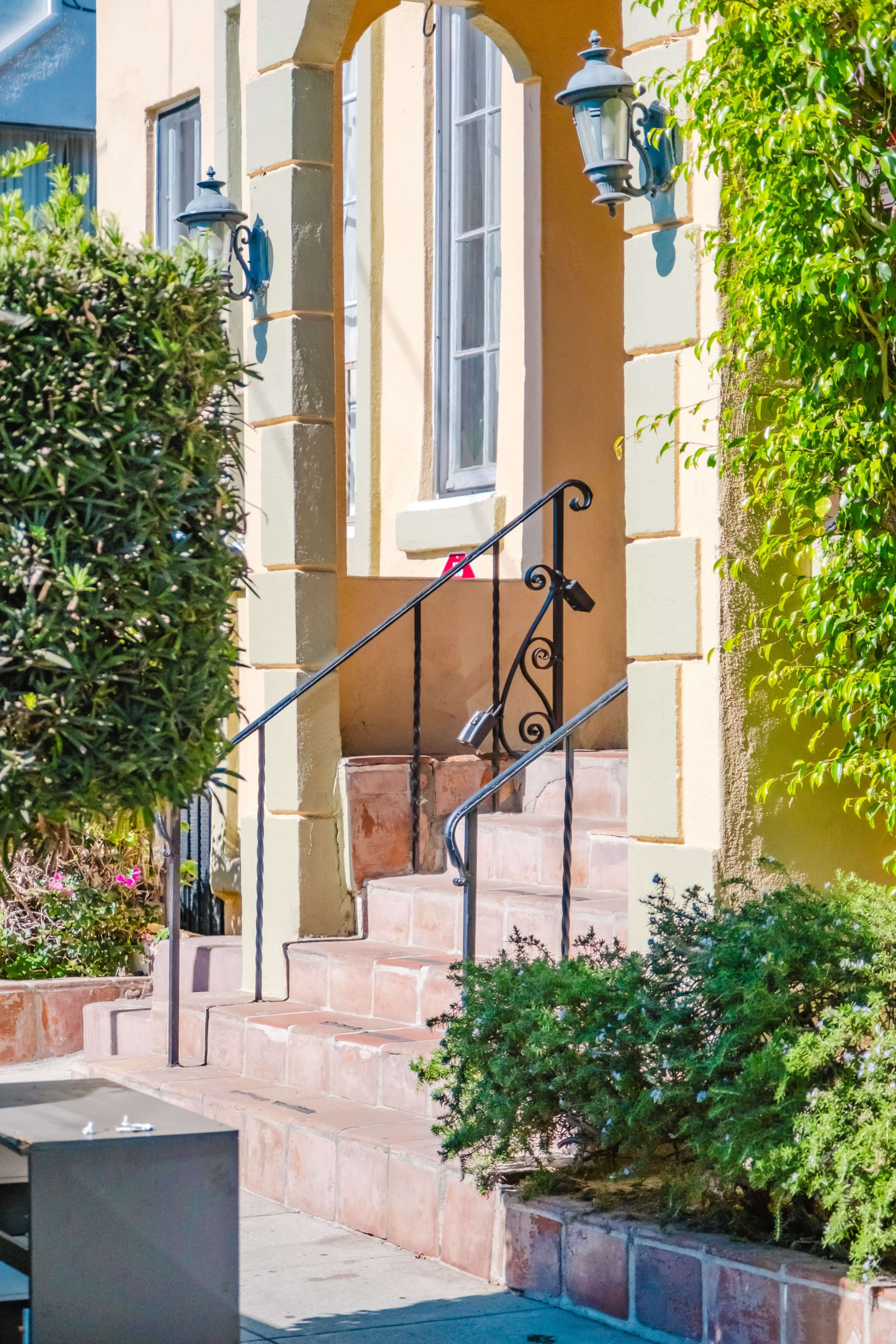 A set of stone steps leads to a yellow building with decorative lanterns and green shrubbery on either side.