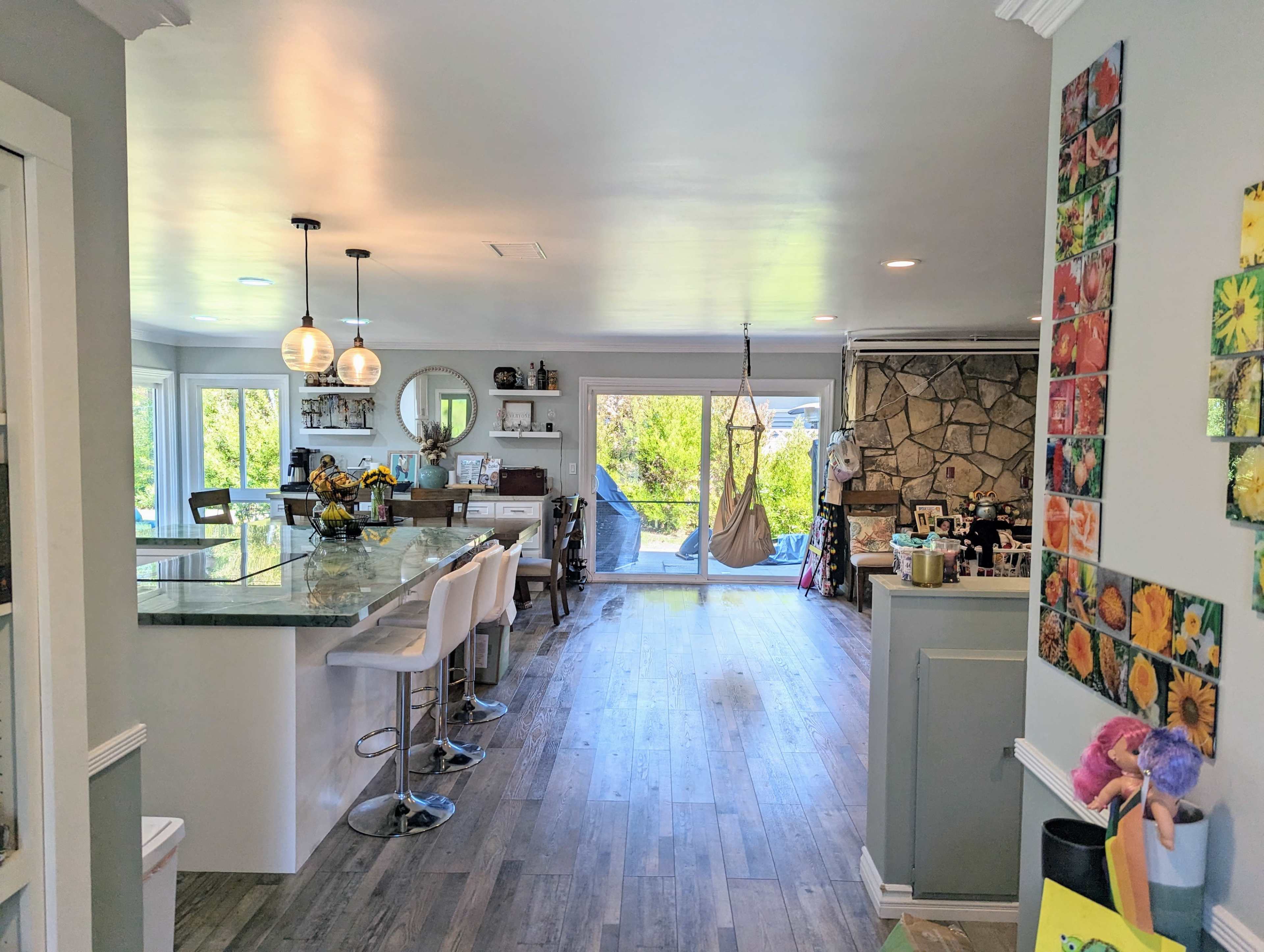 The image shows a spacious, modern kitchen and dining area with a stone wall, glass sliding doors, and a hanging chair.