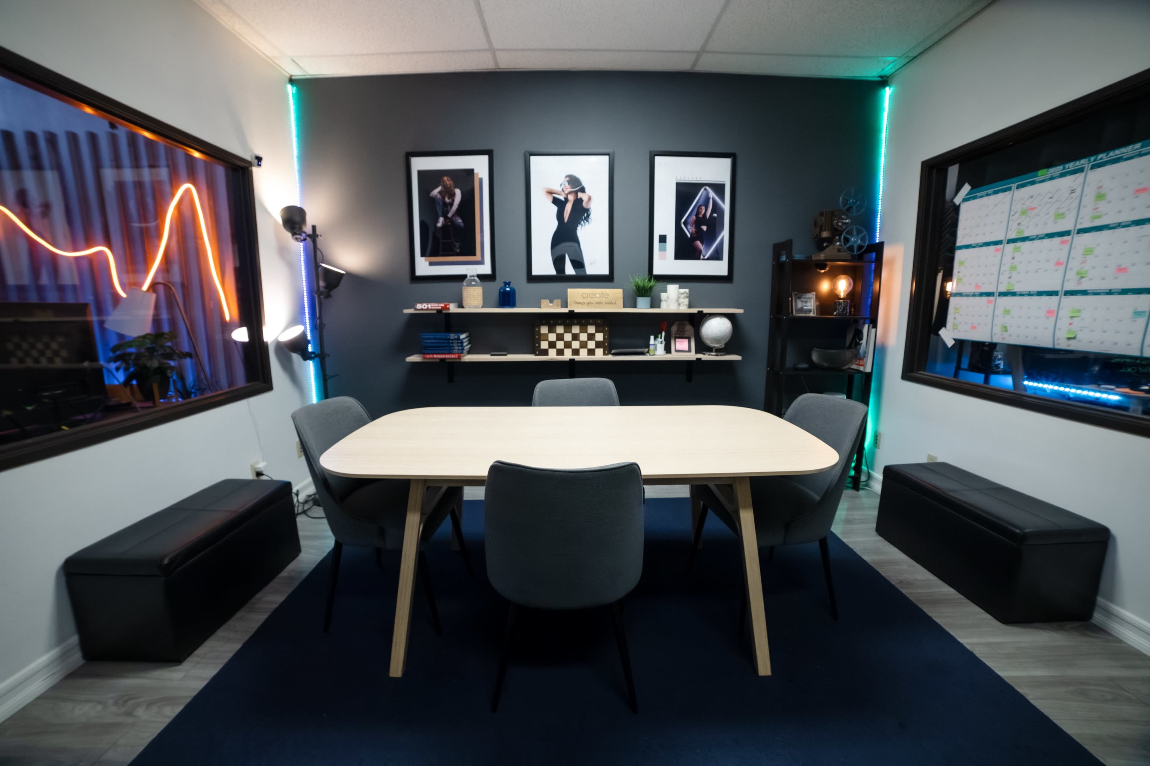 The image shows a modern conference room with a round wooden table surrounded by gray chairs, framed photographs on the walls, and a calendar in the background.