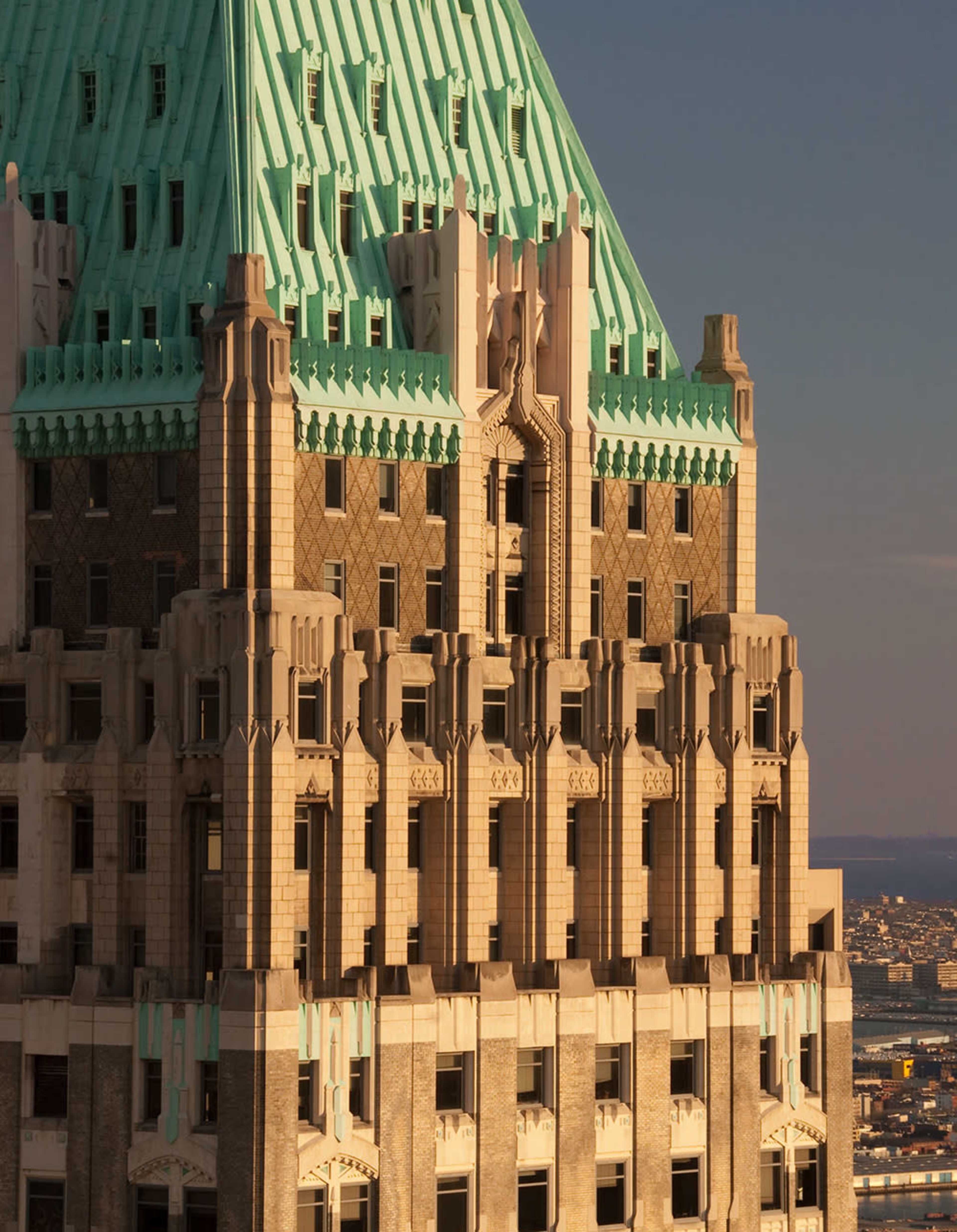 The upper portion of a historic skyscraper featuring a green copper roof and intricate architectural details.