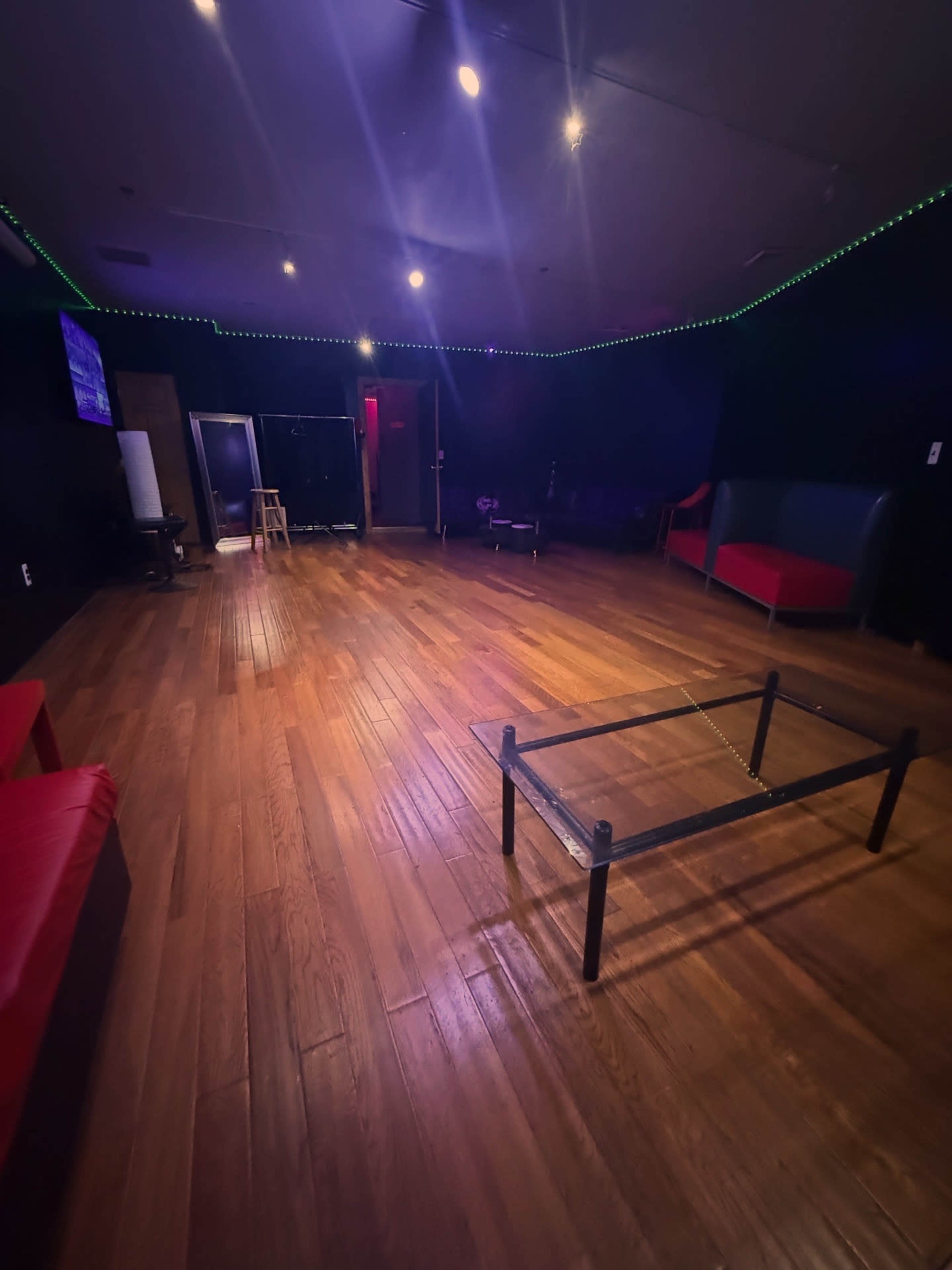The room features polished hardwood floors, black walls, and minimal furniture, including a table and several seating areas.