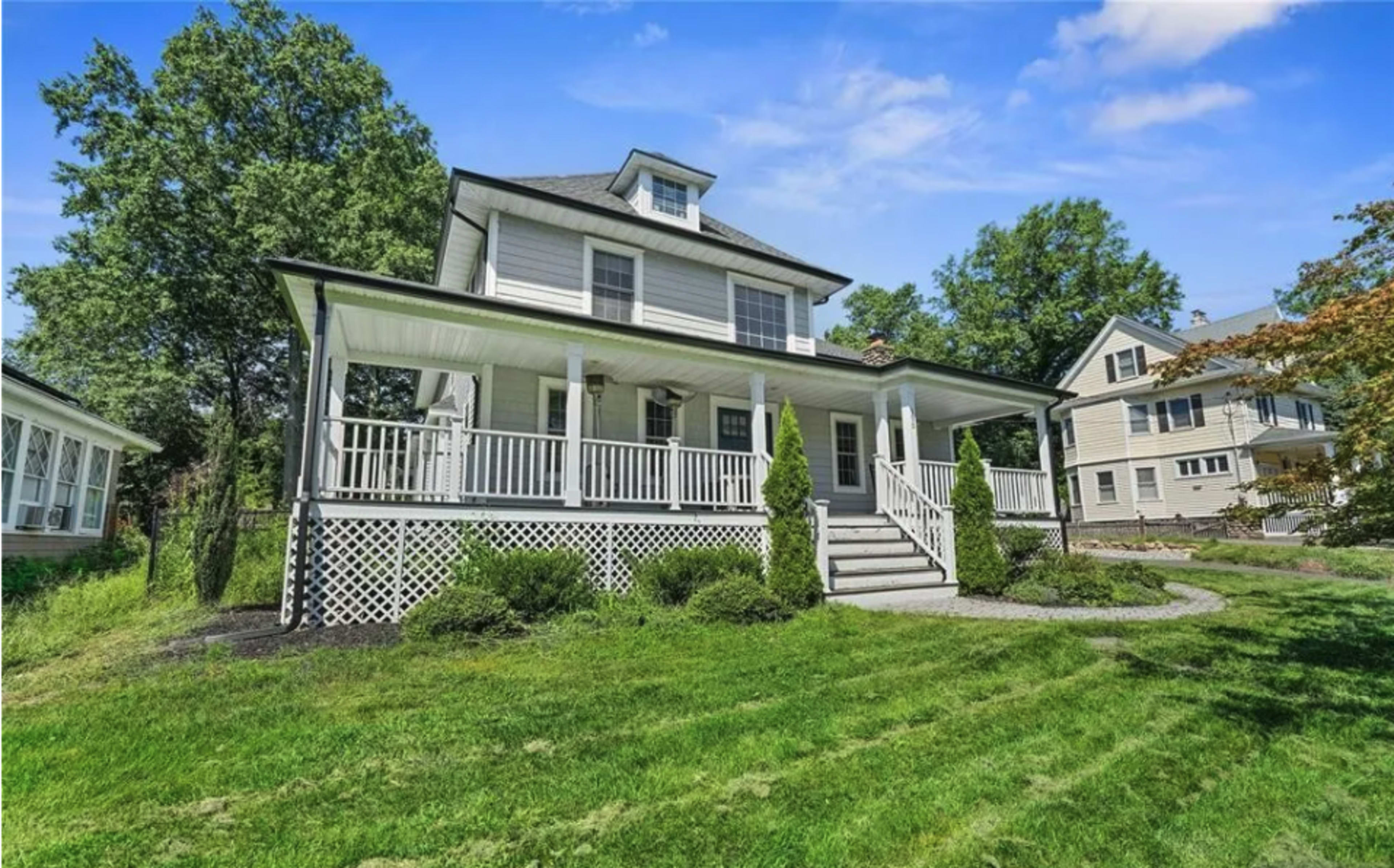 The image shows a two-story house with a front porch, surrounded by a lawn and neighboring homes.
