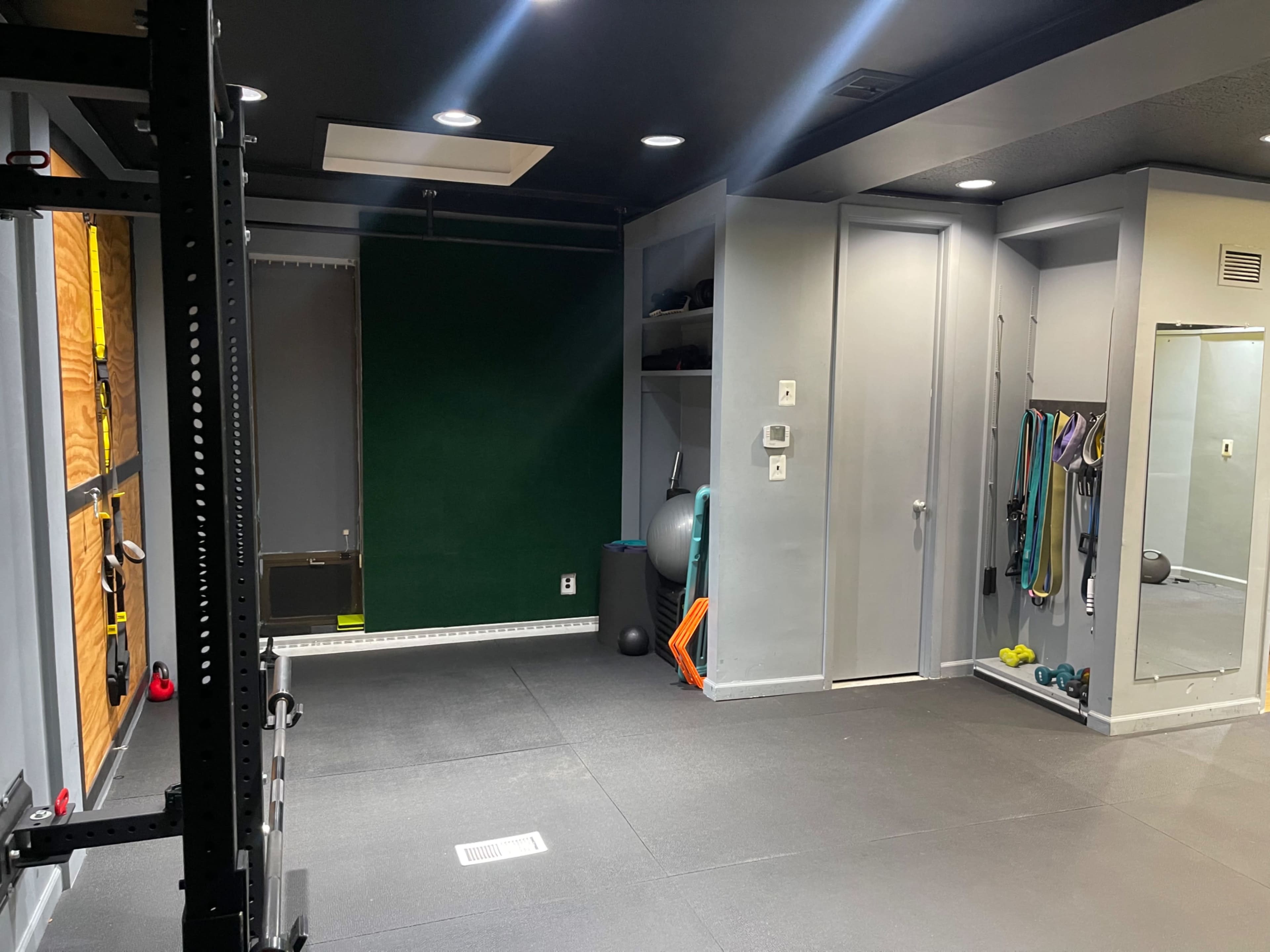 A gym with exercise equipment, including a wall-mounted structure, weights, and fitness accessories against a gray wall.