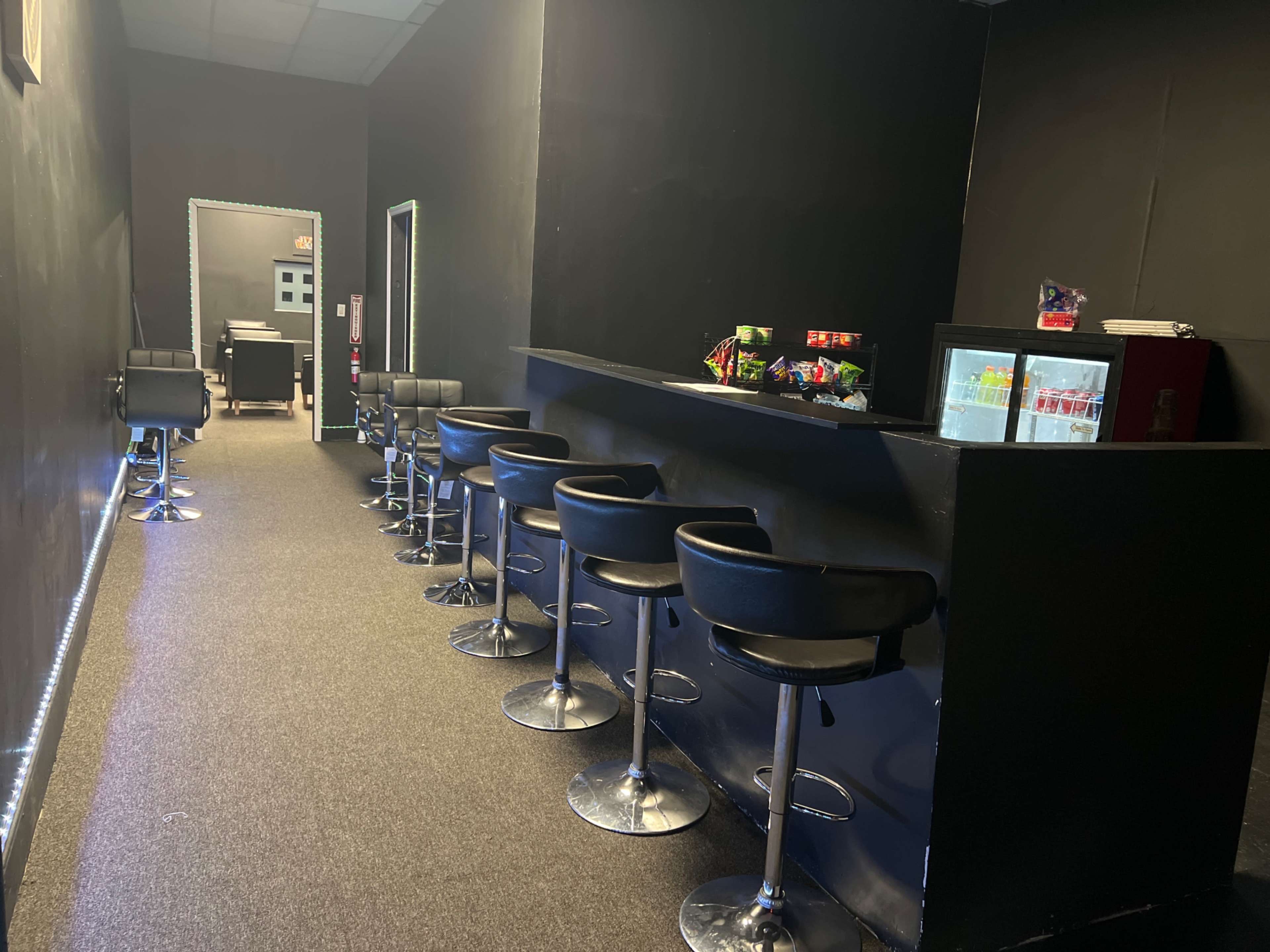 The image shows a narrow room with a bar counter and high stools along one side, leading to a darker area at the back.