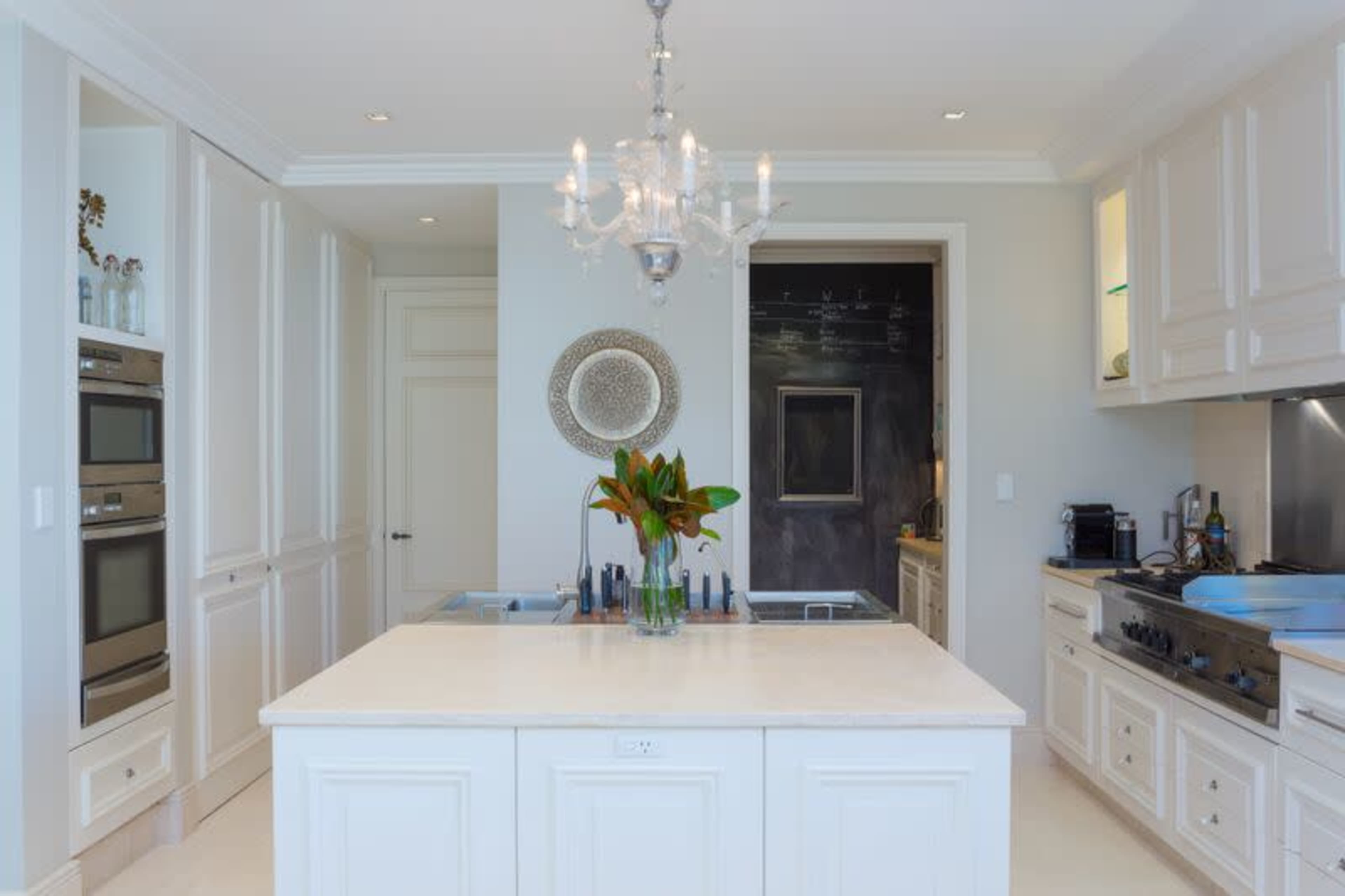 A modern kitchen features an island with a chandelier overhead, built-in ovens, and sleek cabinetry.