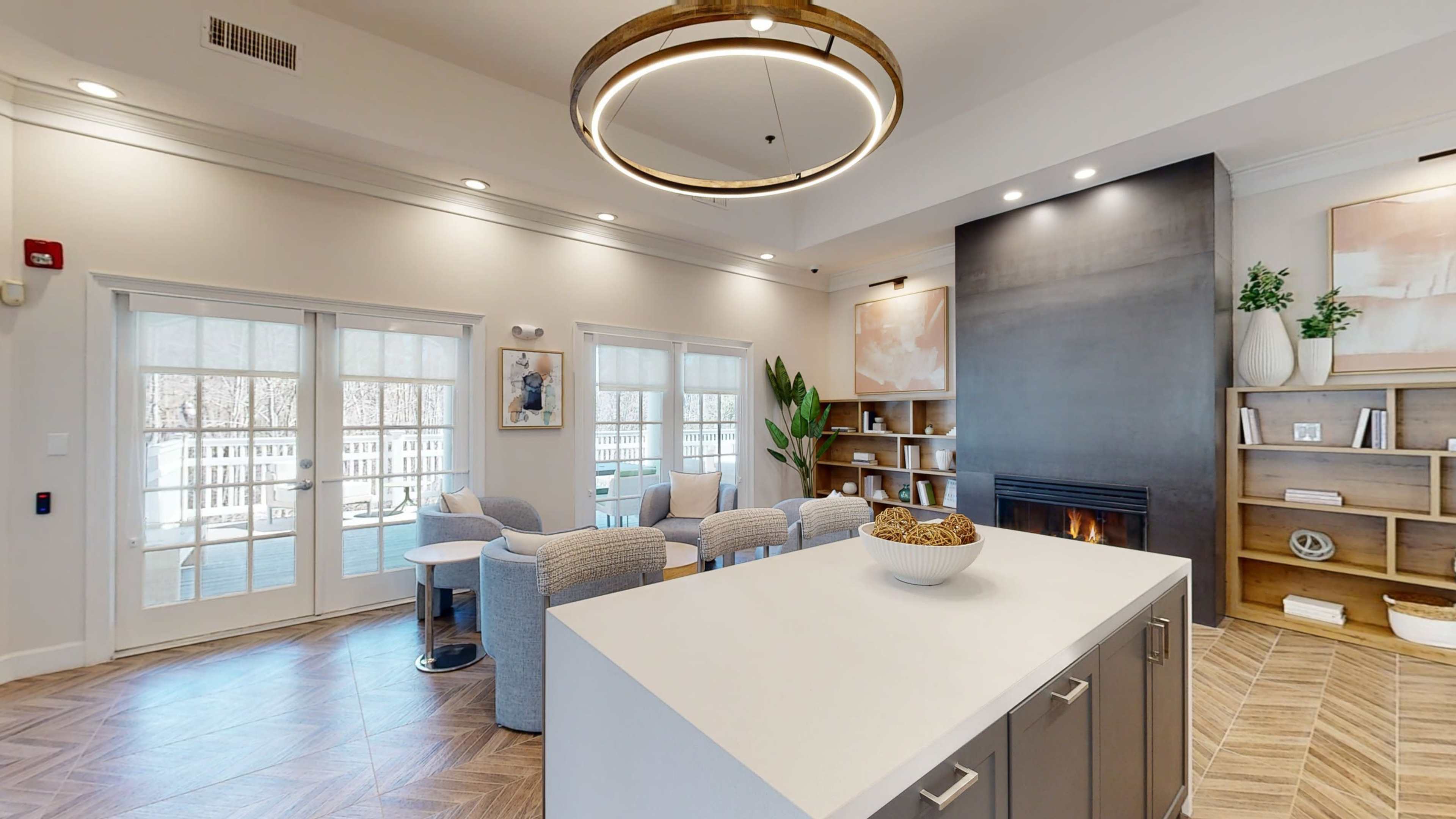 The image depicts a modern living space featuring a well-lit area with a cozy seating arrangement, a fireplace, and a kitchen island with a bowl of snacks.