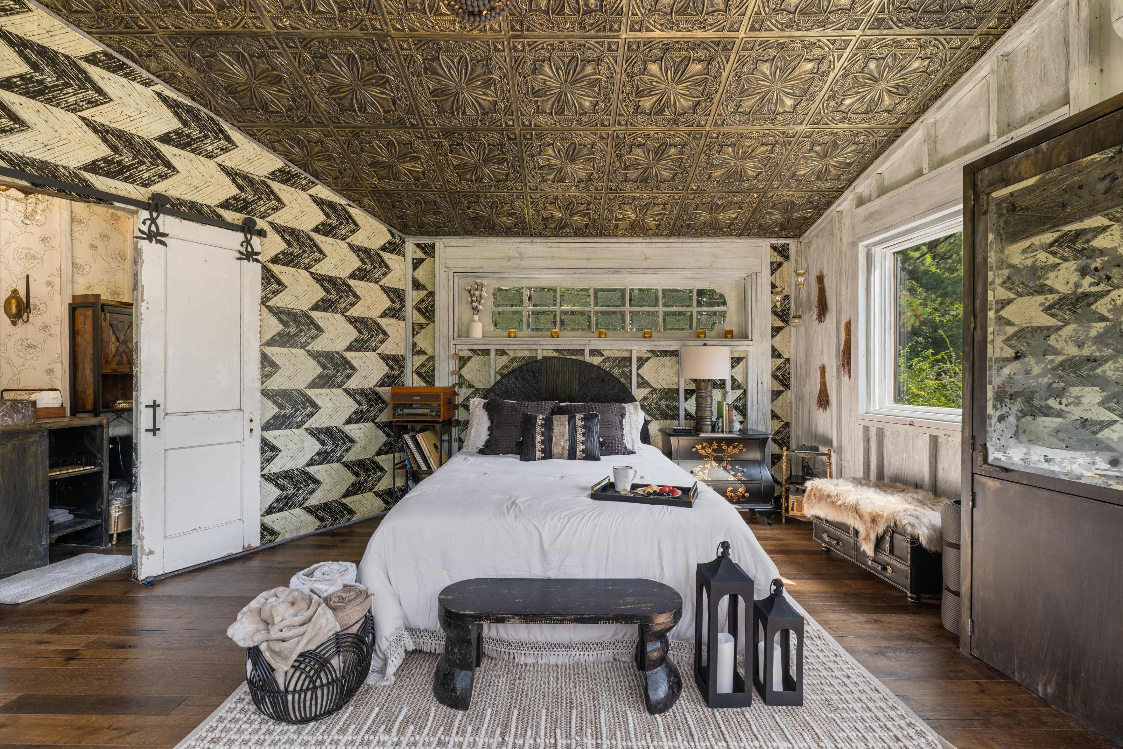 A beautifully designed bedroom featuring a patterned wall, a large bed with decorative pillows, and a mix of rustic and modern furniture.