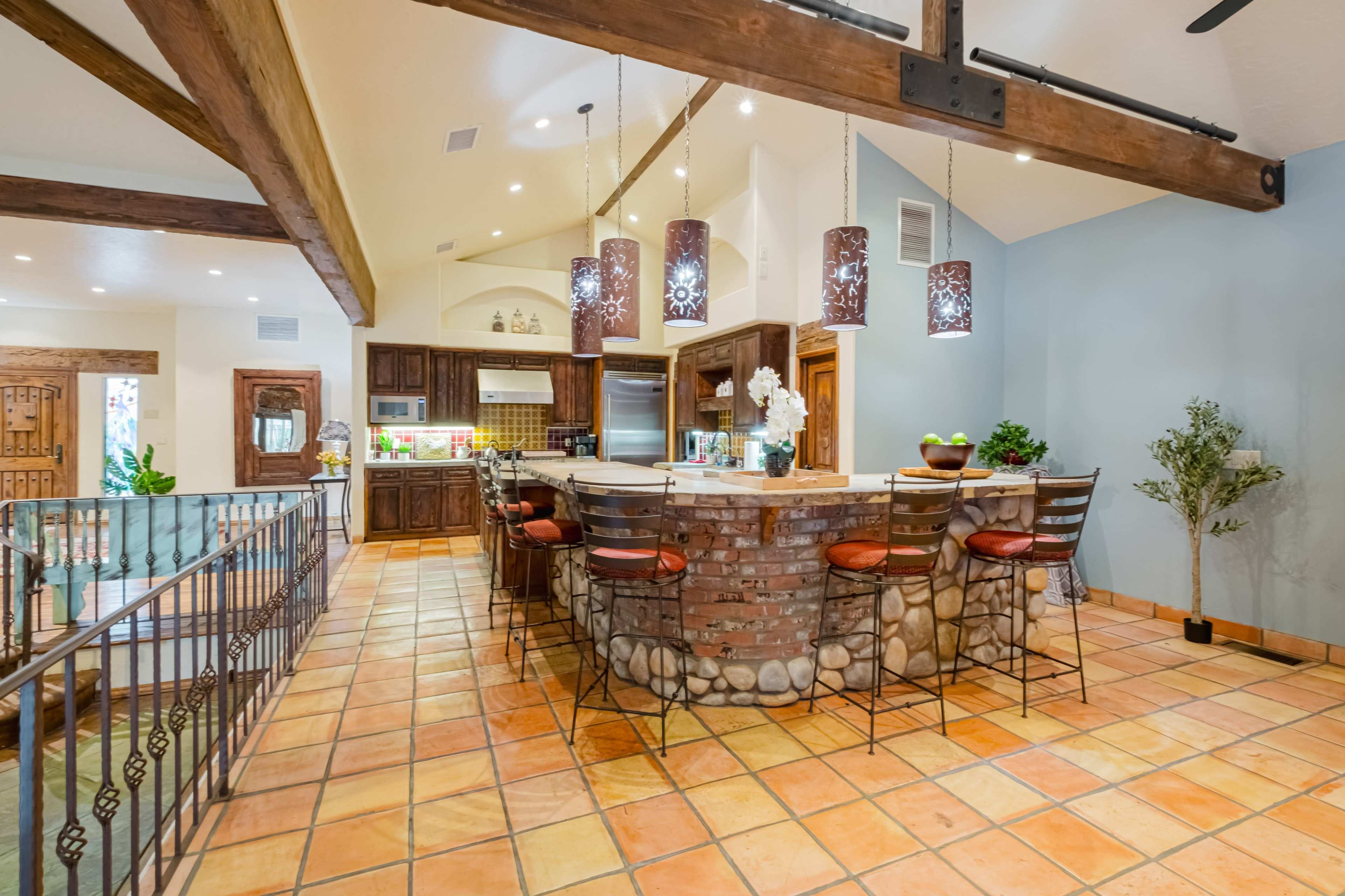 A spacious kitchen featuring a large island with a brick and stone design, surrounded by barstools, and wooden beams overhead.
