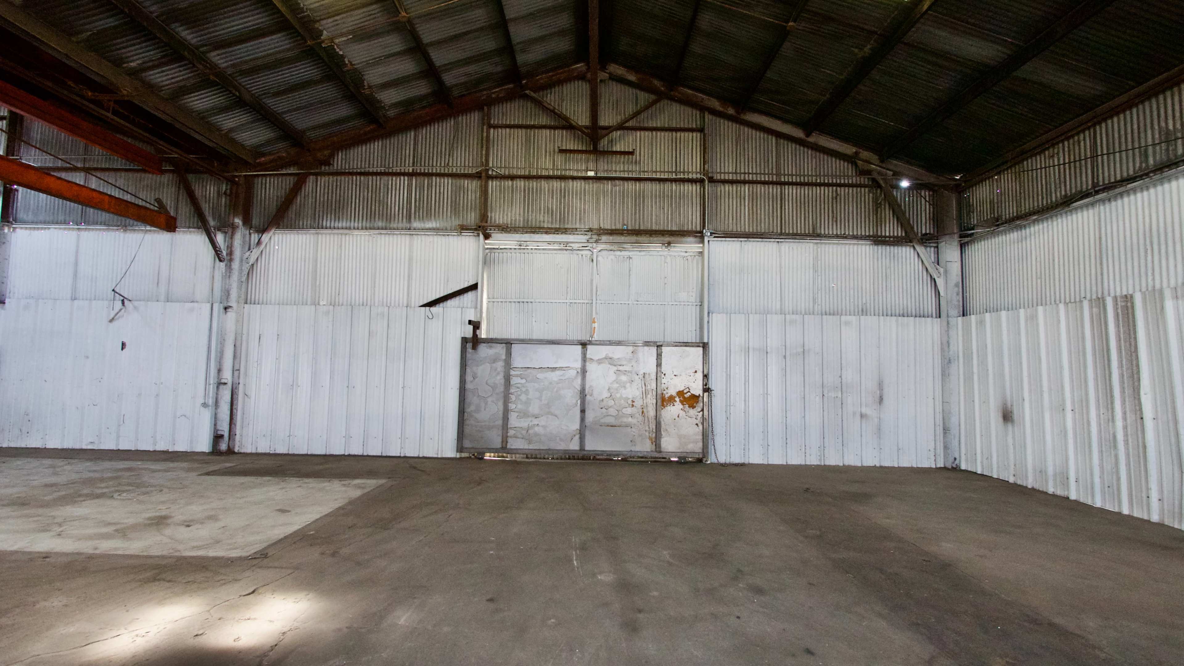The interior of a large, empty warehouse with a metal door at one end and industrial metal walls.