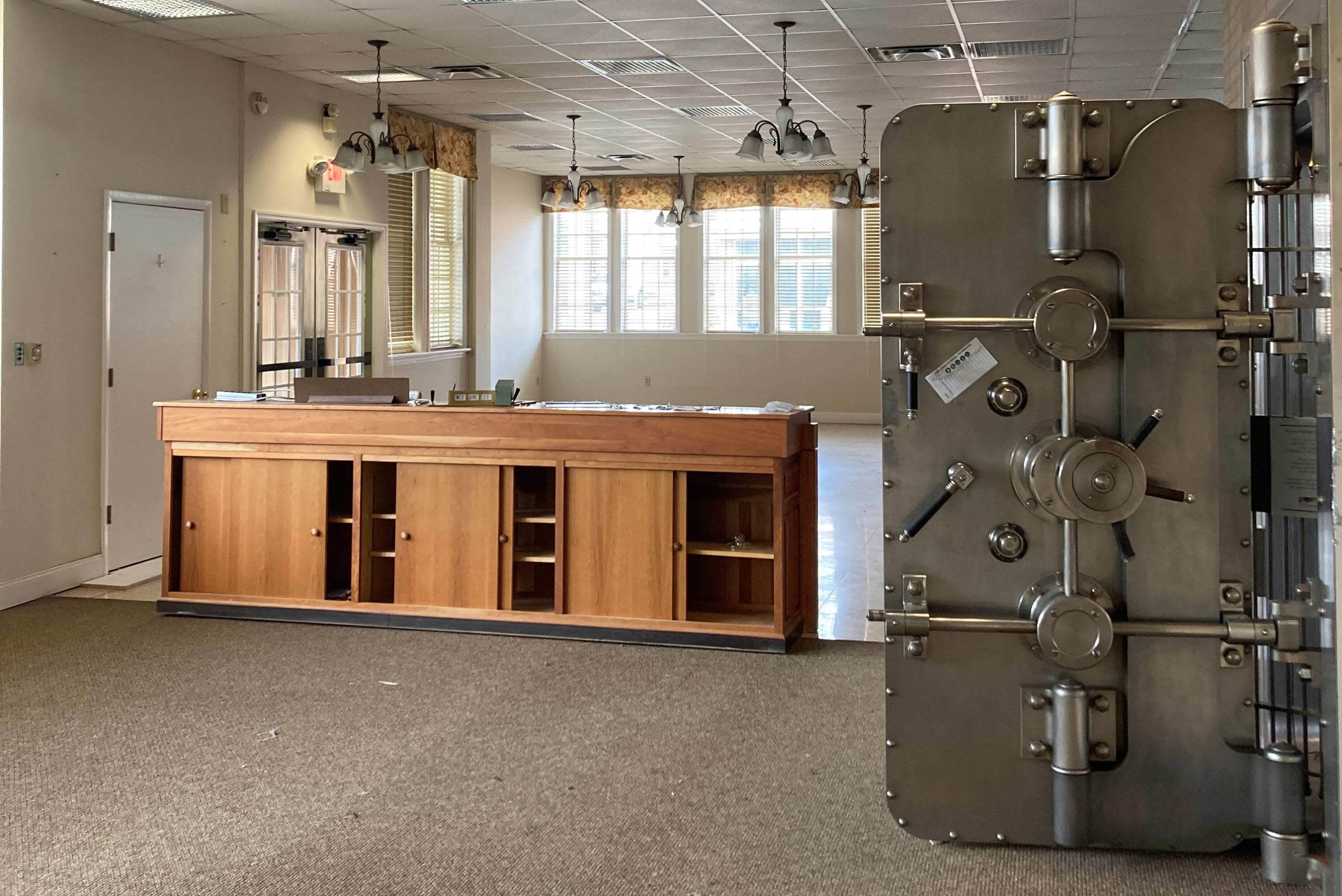 An empty room with a wooden reception desk on the left and a large metal safe on the right.