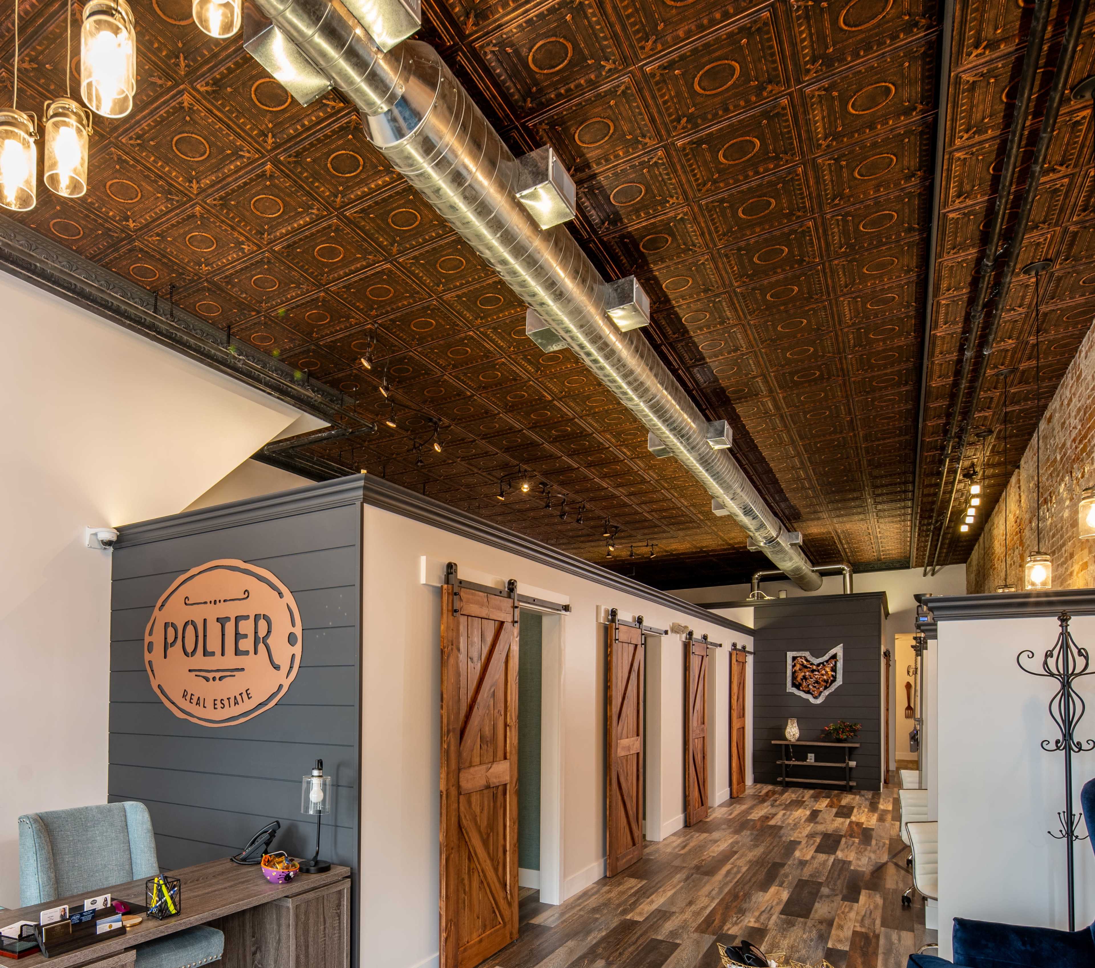 A modern real estate office featuring wooden sliding barn doors, a decorative ceiling, and contemporary lighting.