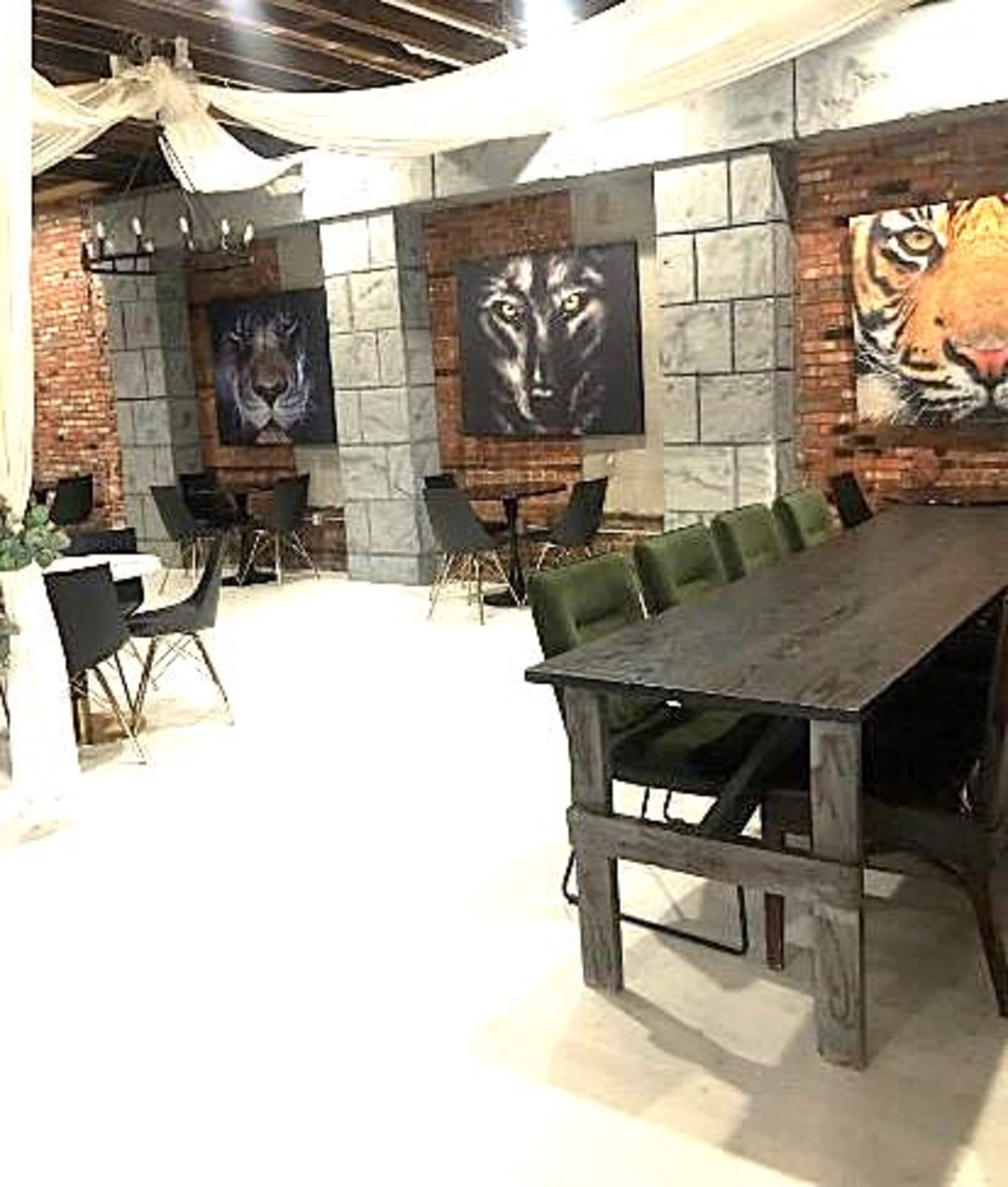 The interior features a dining area with a long black table and green chairs, complemented by large portraits of lions and a tiger on the stone and brick walls.