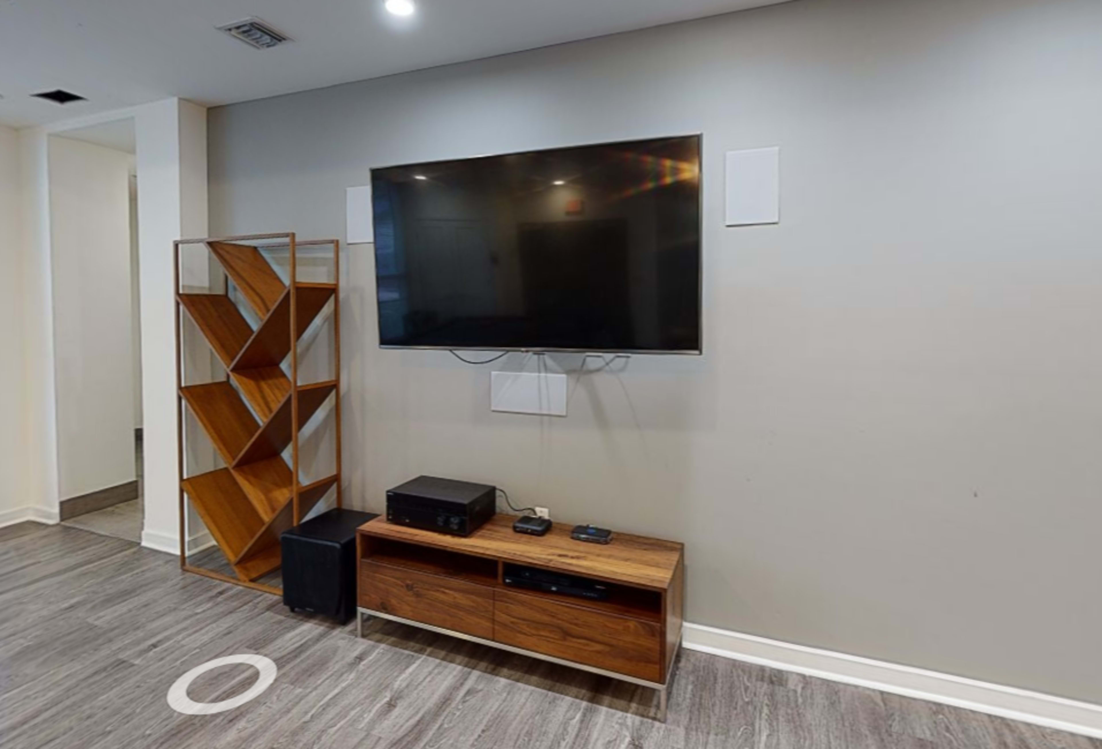 A modern living room setup featuring a wall-mounted television above a wooden media console and a geometric wooden bookshelf.