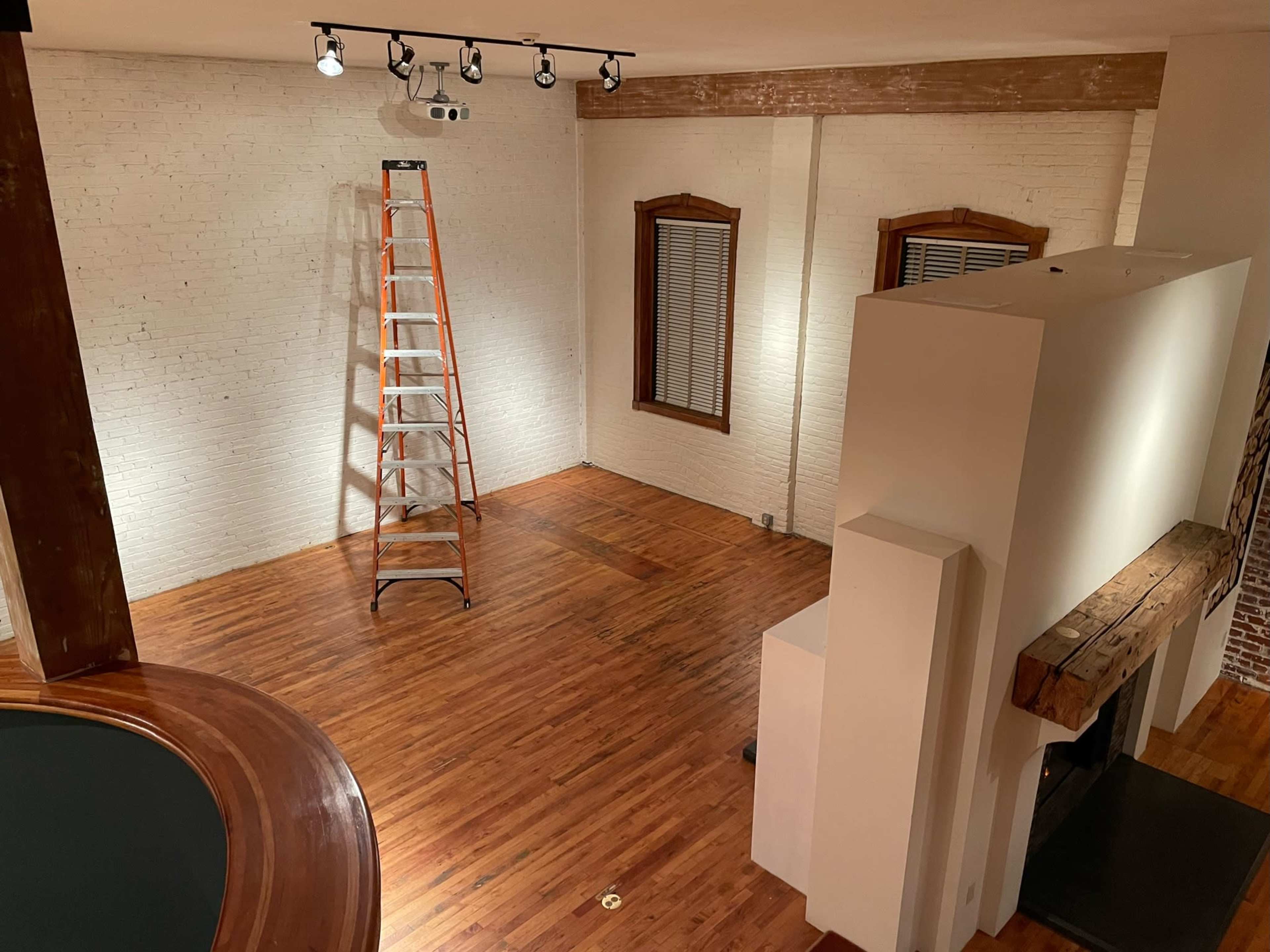 An empty room with hardwood floors features a ladder, a projector mounted on the ceiling, and bare walls.