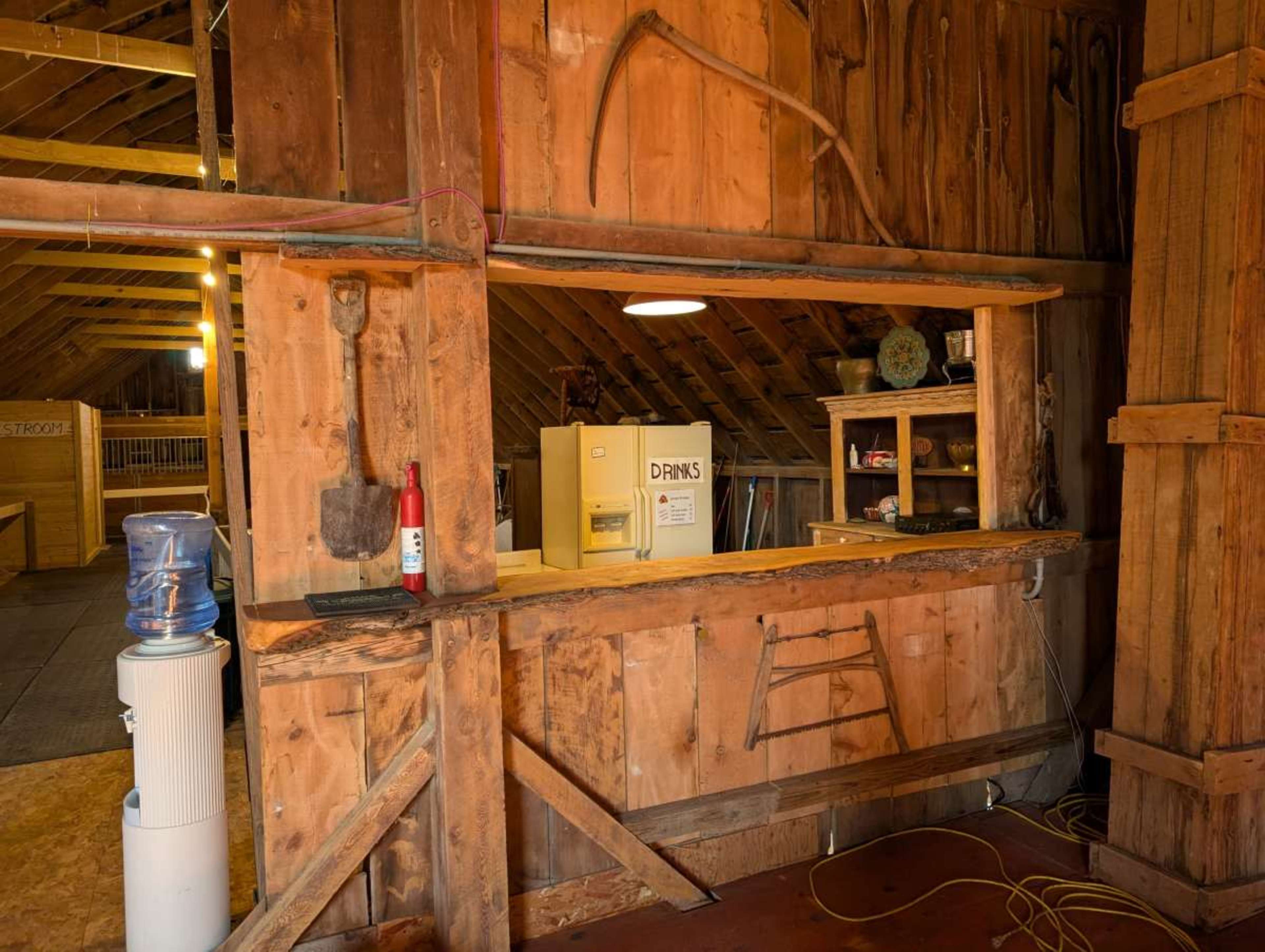 The image shows a wooden barn interior featuring a service counter with a water cooler and various tools displayed on the walls.