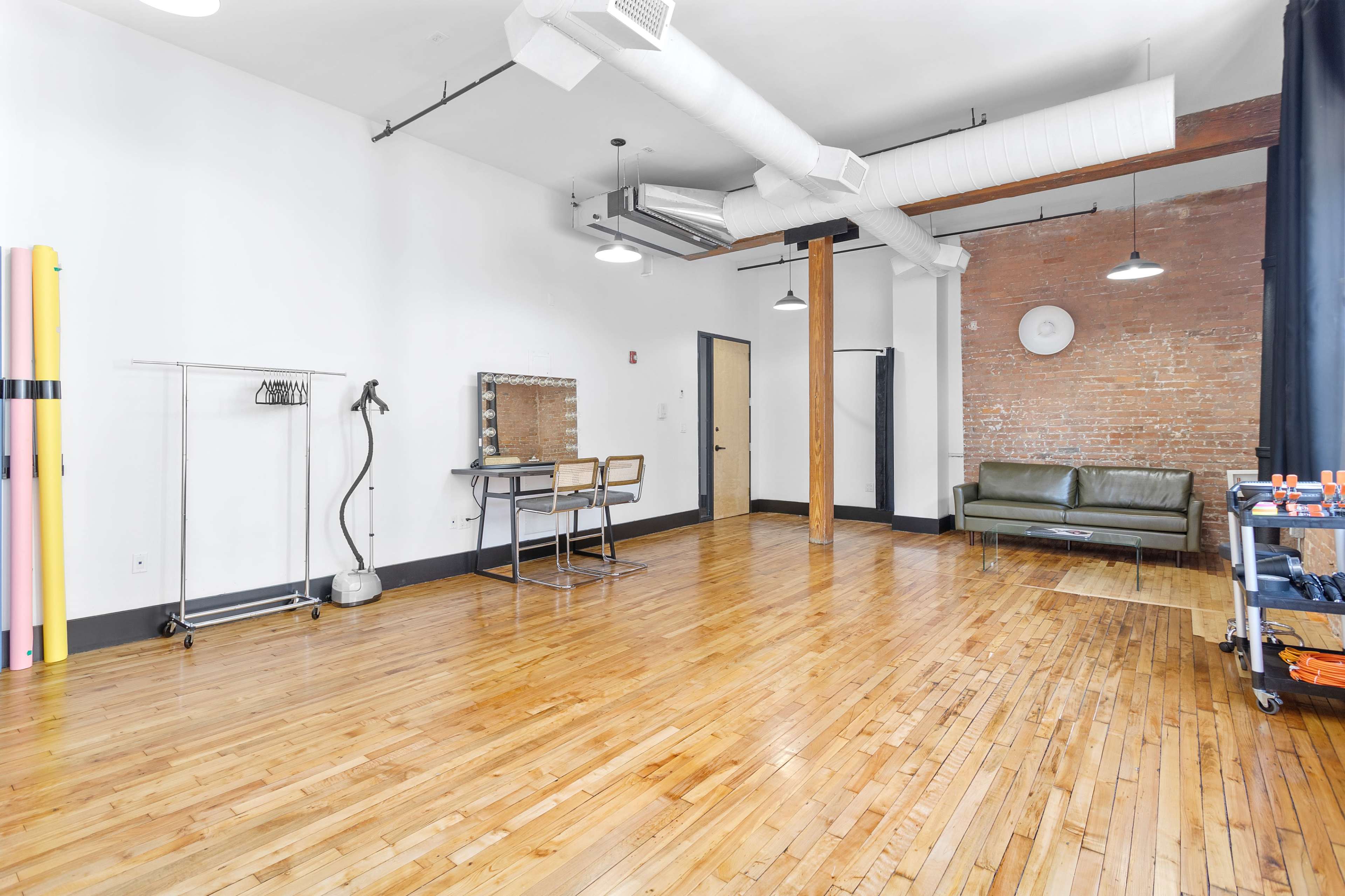 A spacious room features hardwood floors, a green sofa, a dressing mirror, and a clothing rack along with various equipment.