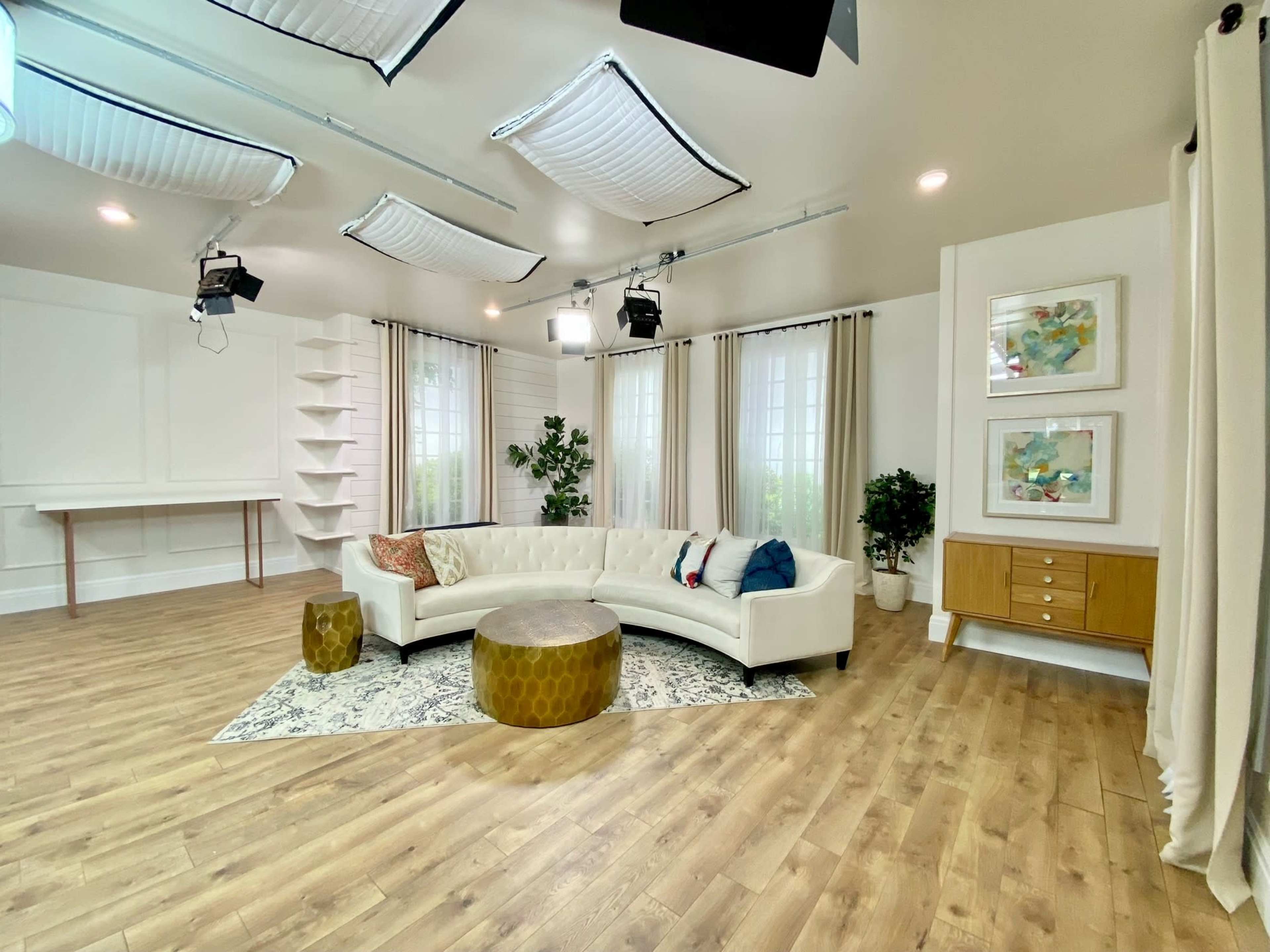A modern living room with a white sectional sofa, a round gold coffee table, and large windows, complemented by plants and decorative artwork.