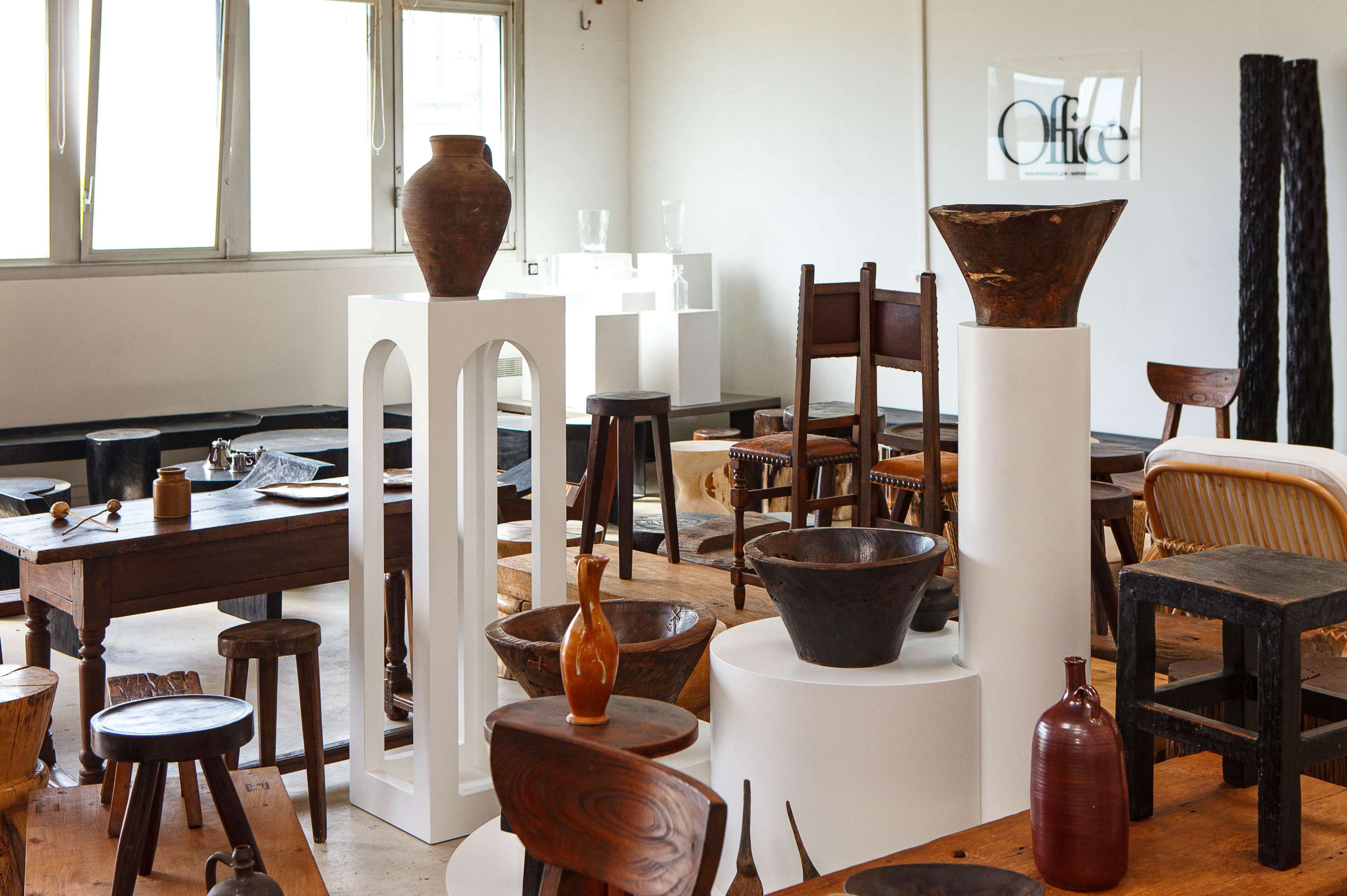 A gallery filled with various wooden furniture and pottery displayed on stands and tabletops in a well-lit, modern interior space.