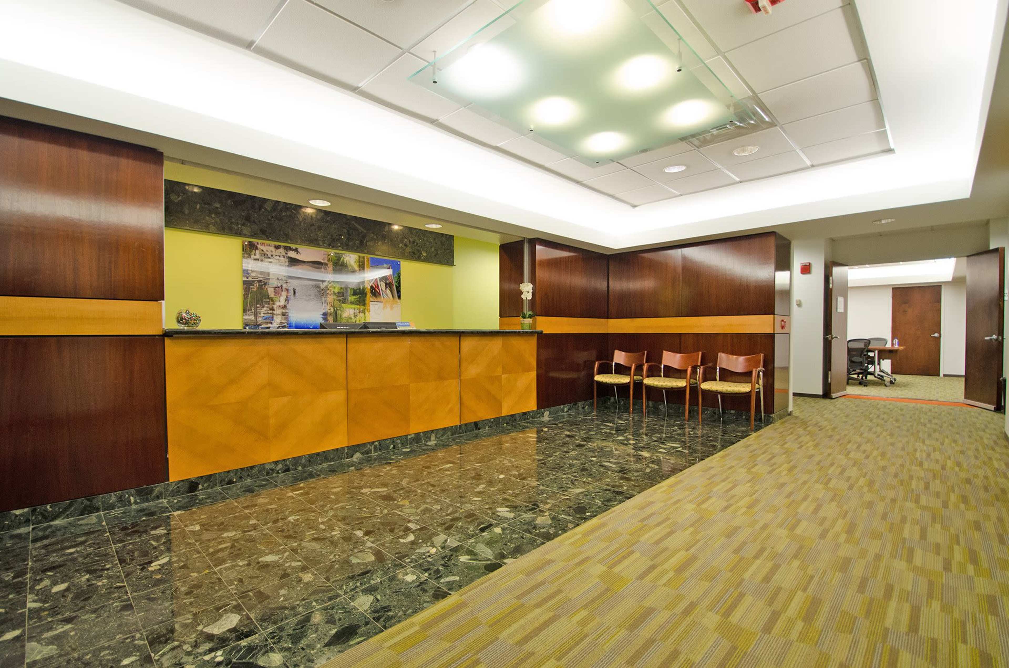 The image shows a modern reception area with a wooden front desk, a green and yellow accent wall, and seating arranged along one side.