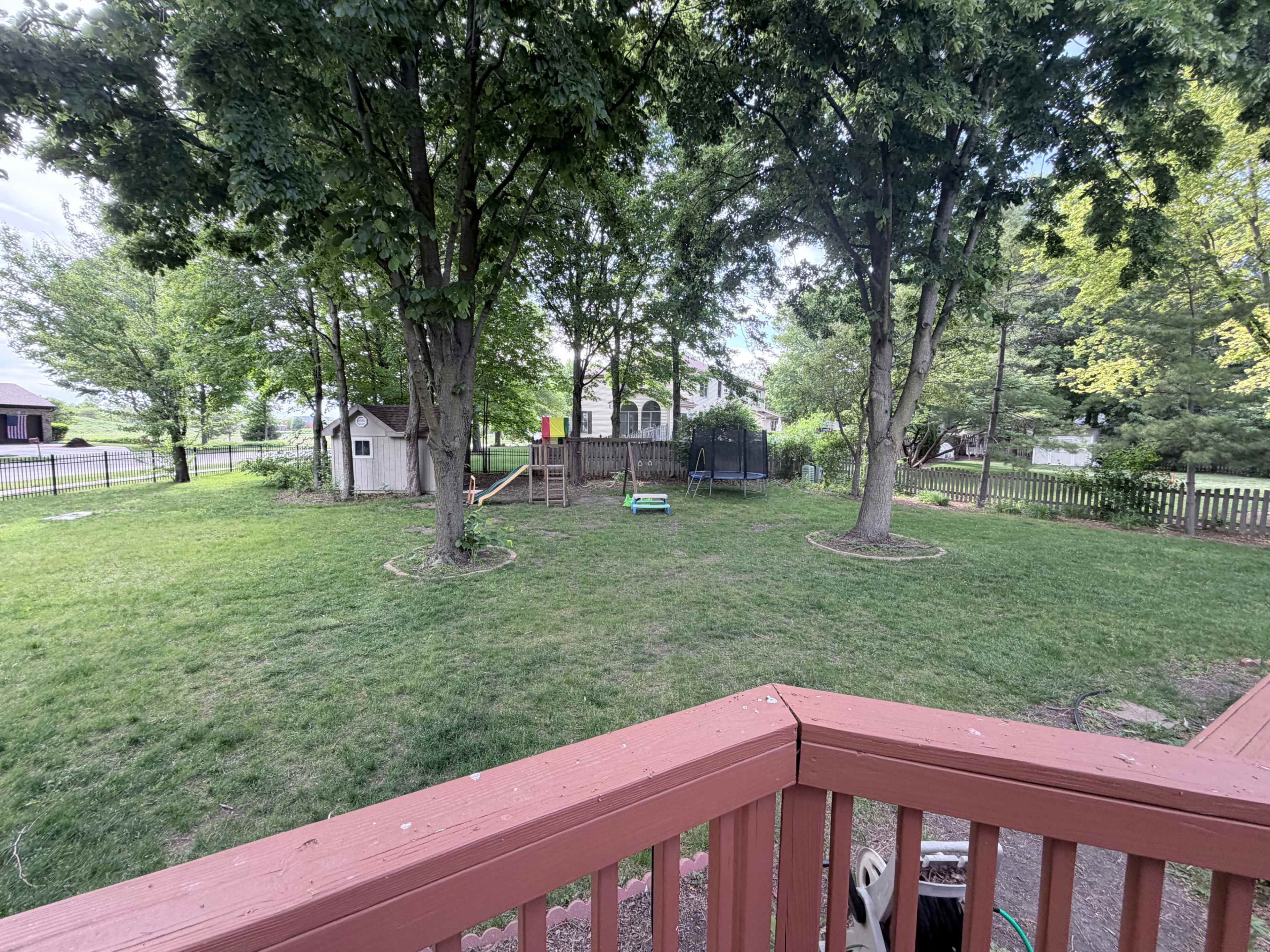 The image shows a grassy backyard with two trees and playground equipment on a deck overlooking the area.