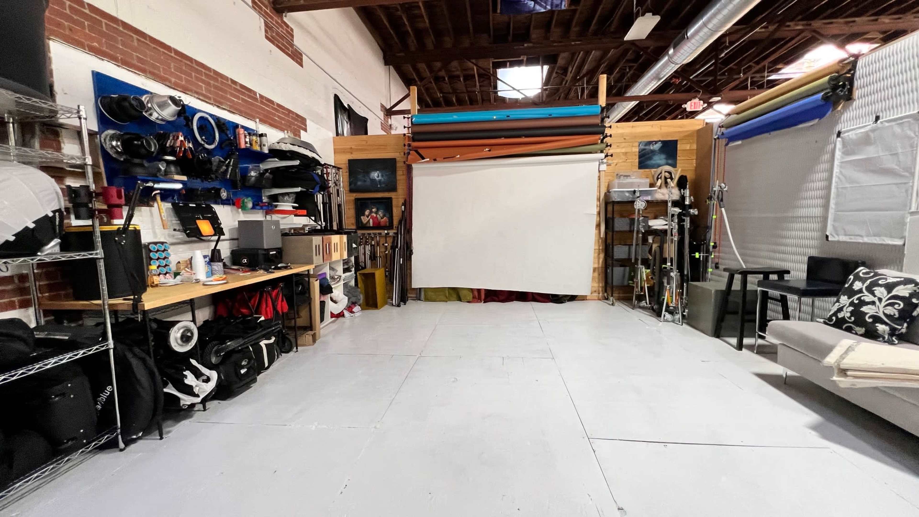 The image shows a spacious studio with organized lighting equipment, backdrops, and a seating area.