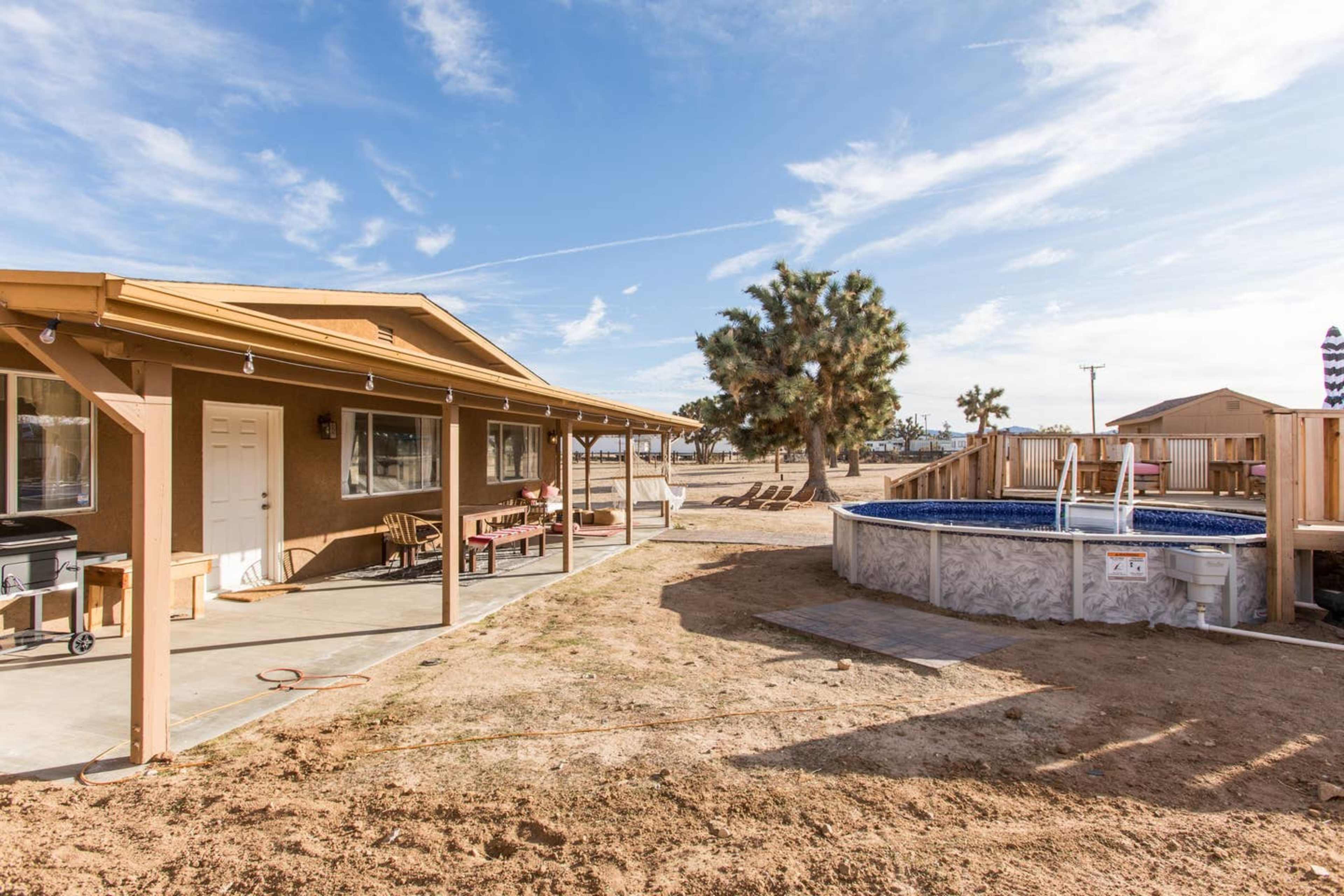 A single-story house with a covered patio, a pool, and a Joshua tree in a desert landscape.