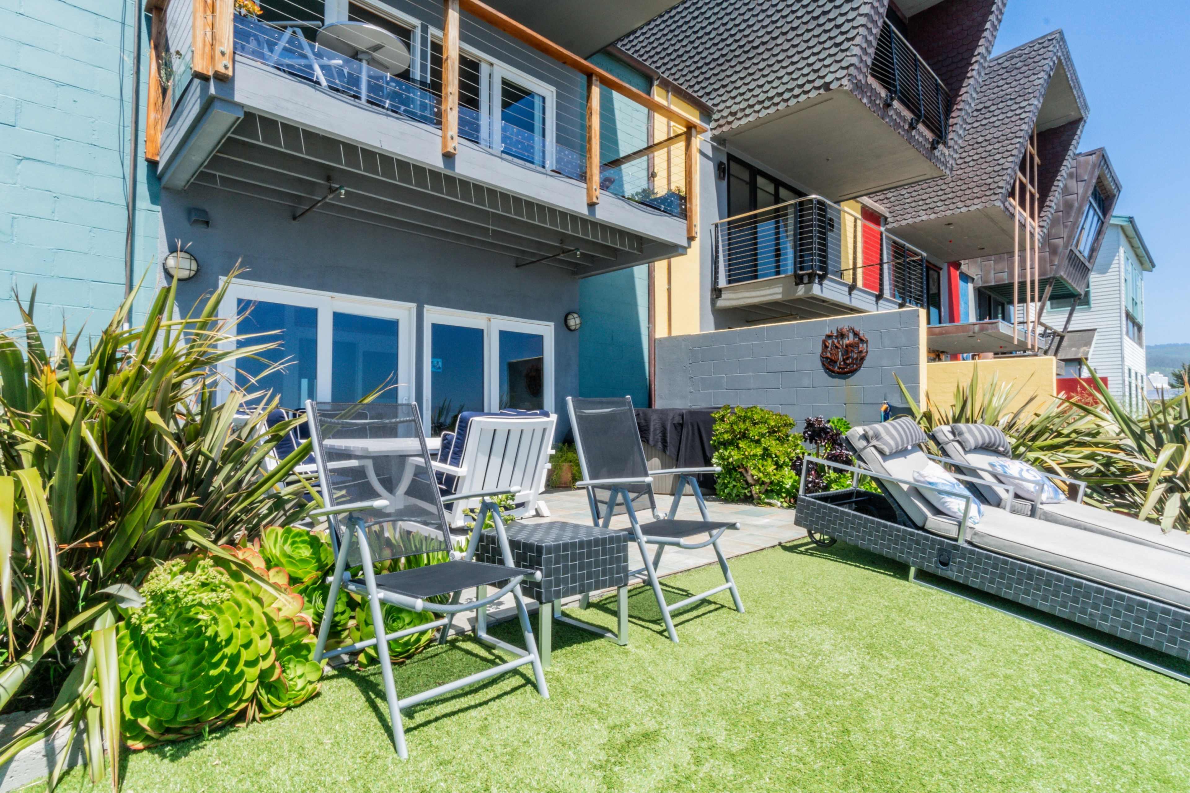The image shows a backyard area with two folding chairs on artificial grass in front of a modern building featuring multiple balconies and colorful exterior walls.