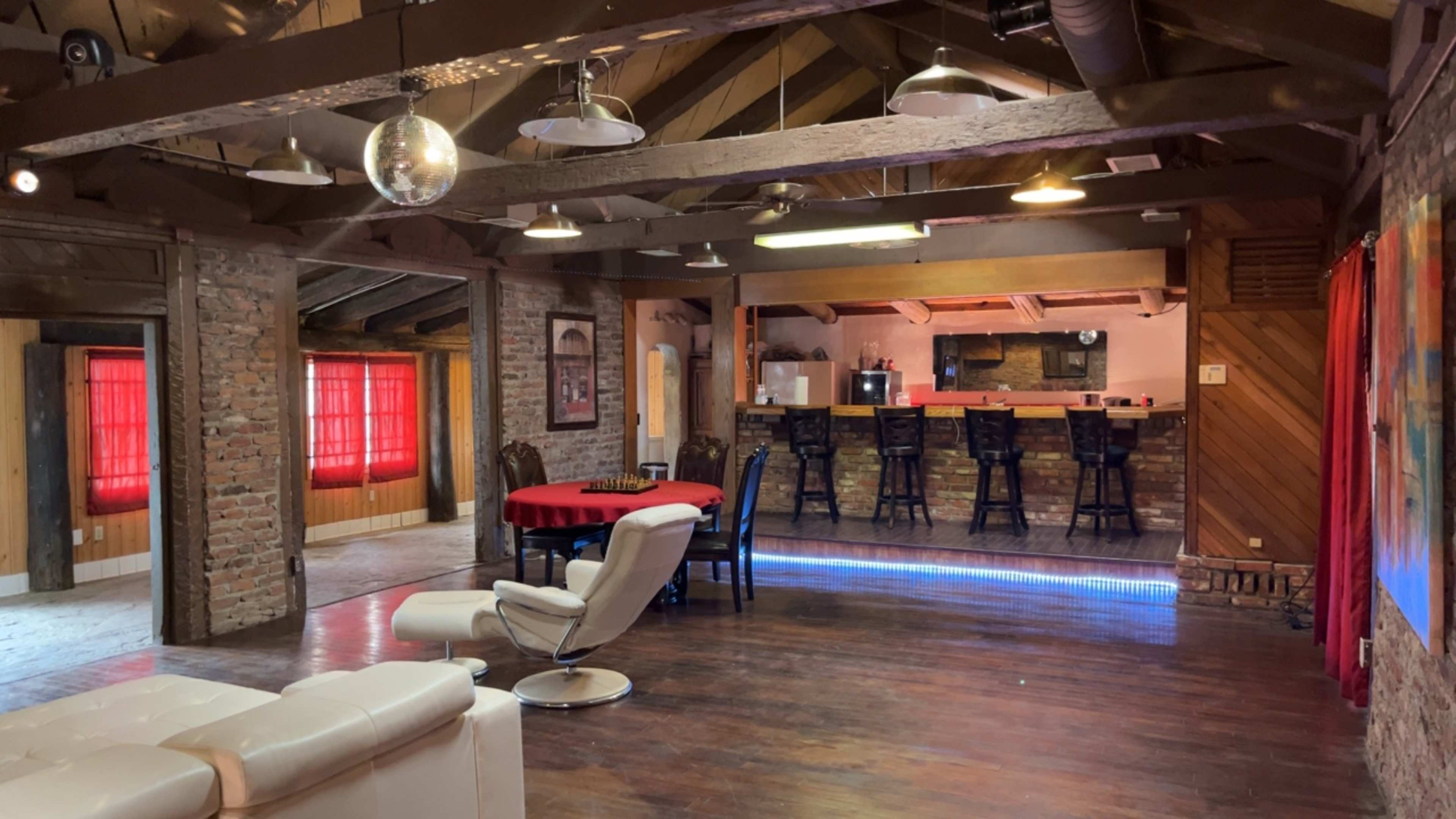 A spacious interior with a bar area, dining table, and seating arranged under exposed wooden beams and a large disco ball.