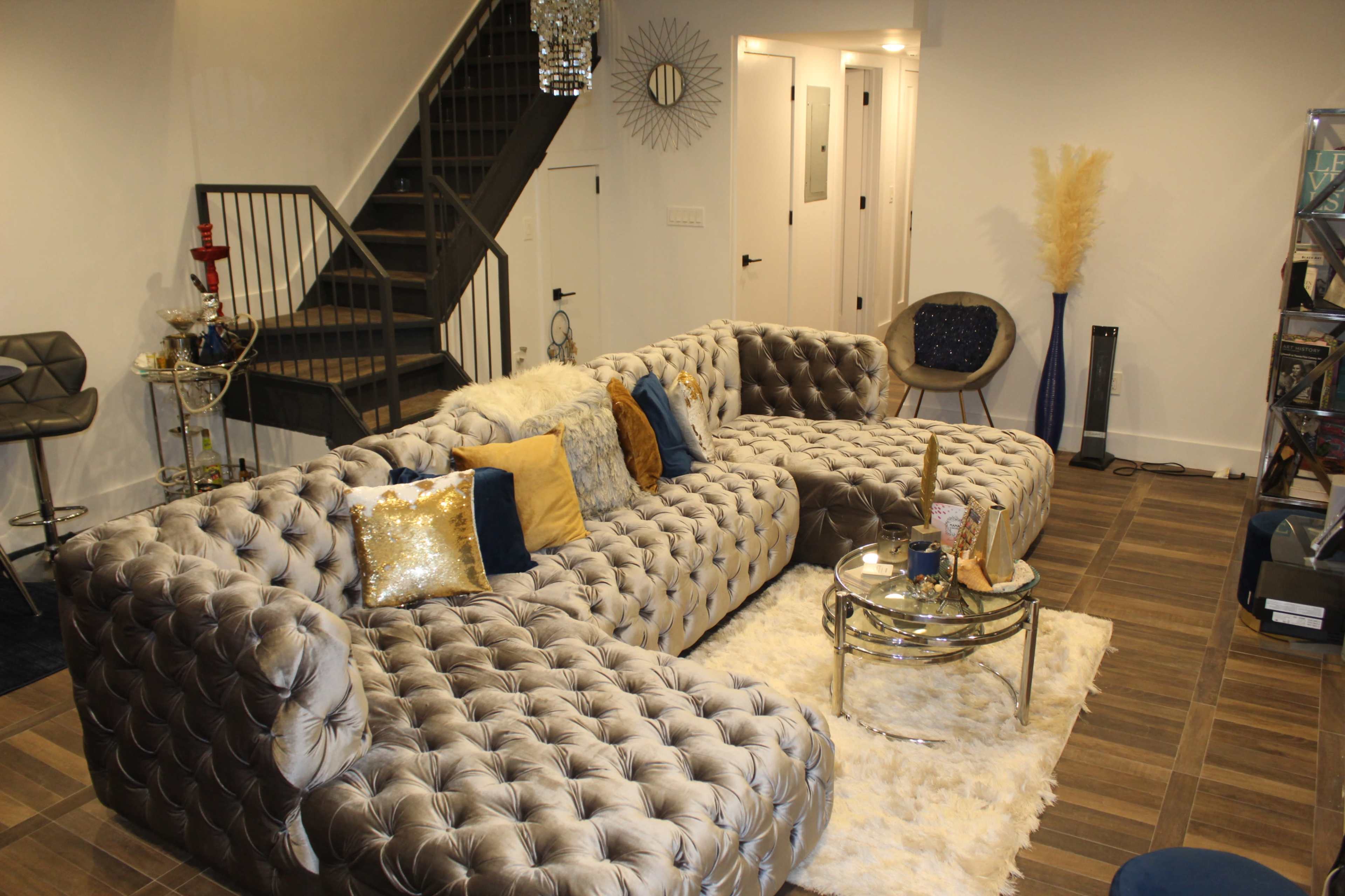 A modern living room featuring a plush, tufted sectional sofa, a glass coffee table, and a staircase in the background.