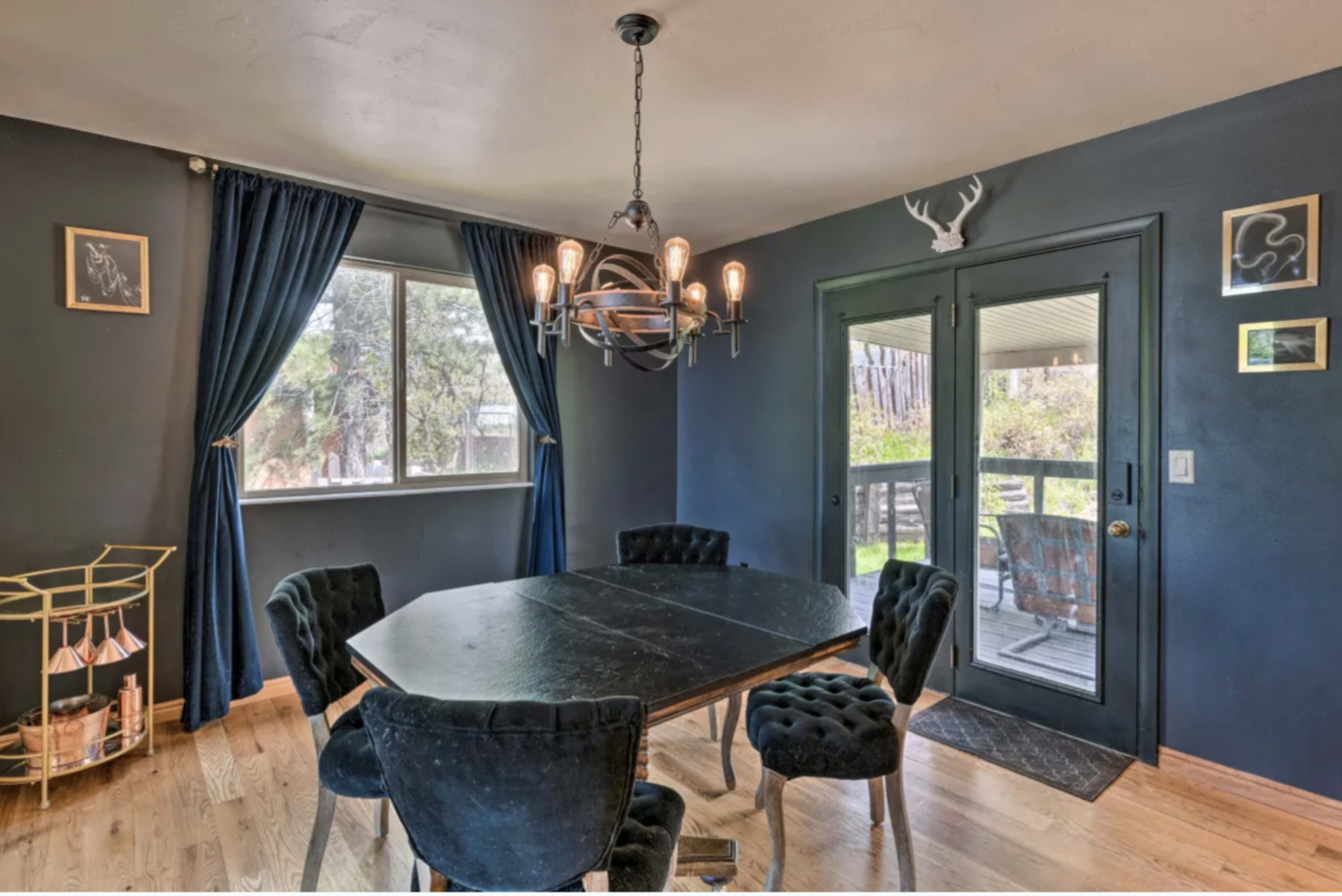 A dining area features a dark blue wall, a round black table surrounded by tufted chairs, and a sliding glass door leading to an outdoor space.