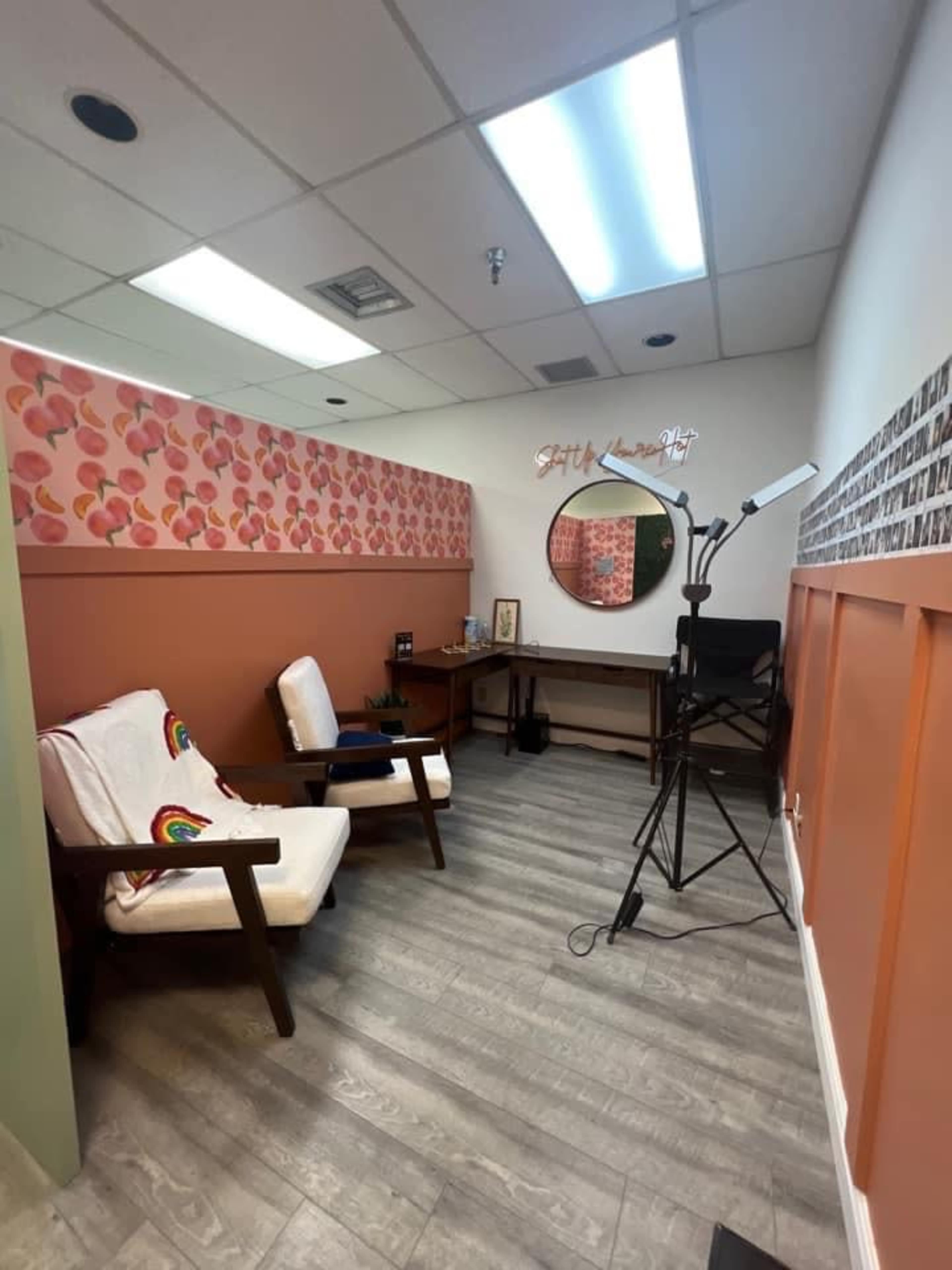 A small, well-lit room with two wooden chairs, a desk, and a ring light set up against patterned walls.