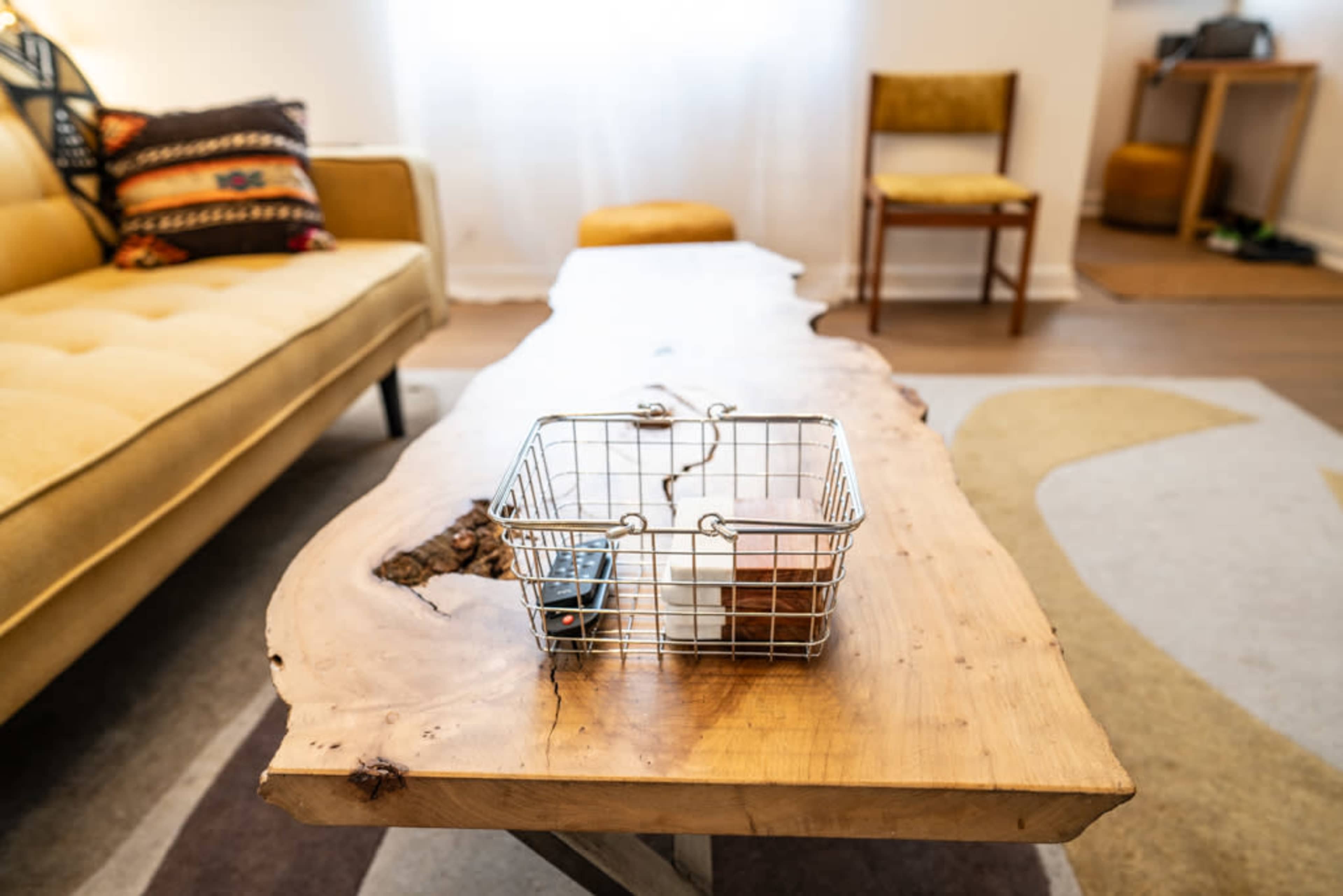 A wooden coffee table with a natural edge holds a metal wire basket in a modern living room.
