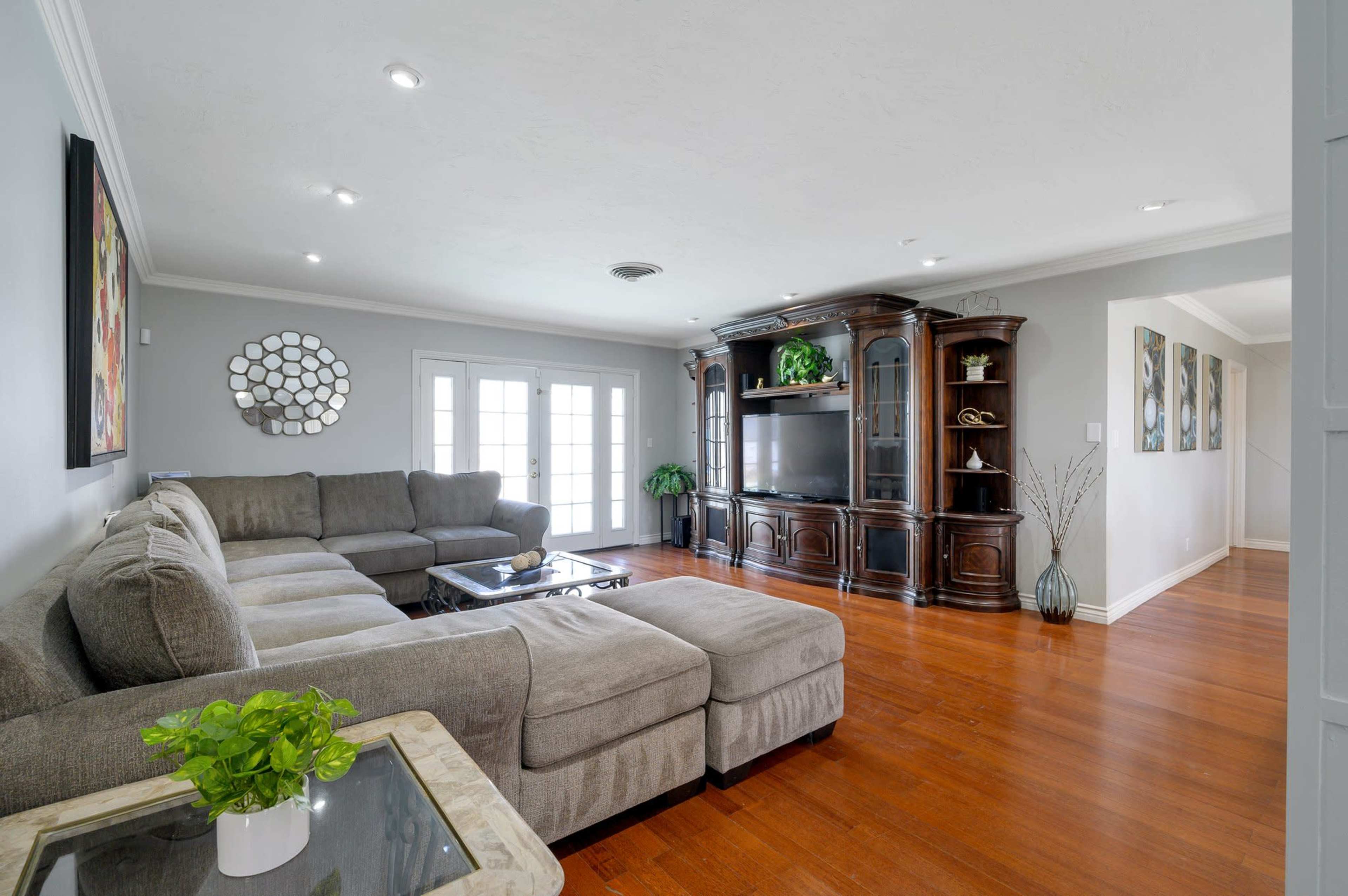 The living room features a large sectional sofa, a wooden entertainment center, and a coffee table, all arranged around a spacious, hardwood floor area.