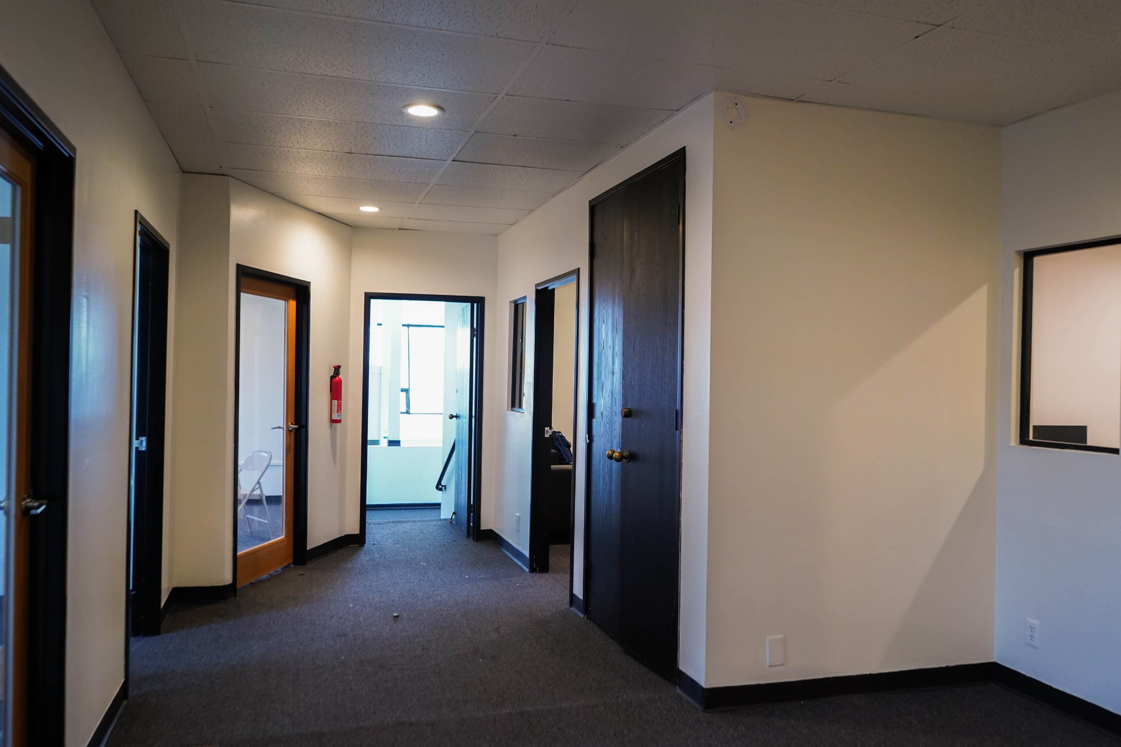 The image shows a hallway with doors on either side, leading to various rooms in a brightly lit office space.