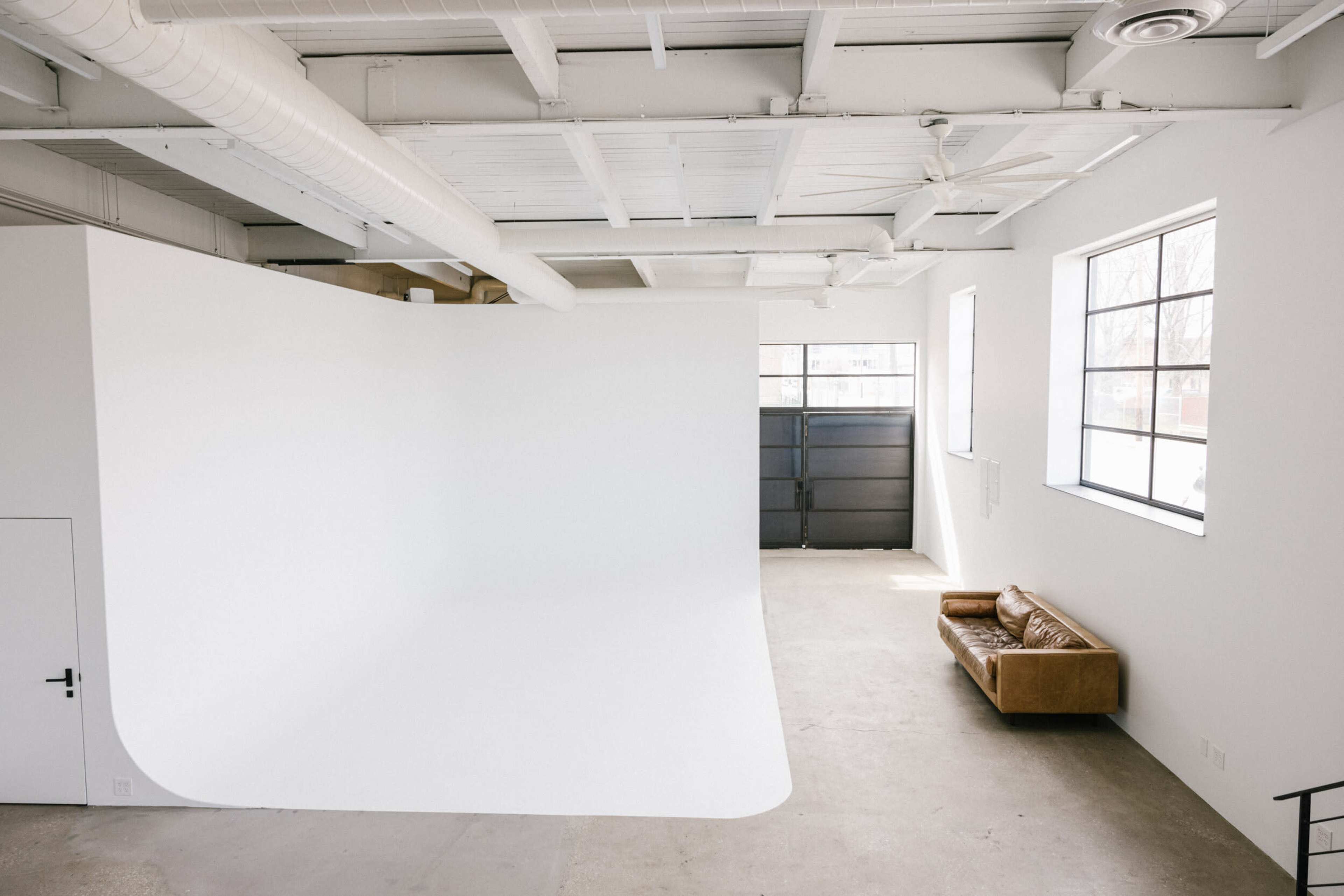 A spacious, well-lit studio with a large white backdrop and a brown leather couch against one wall.