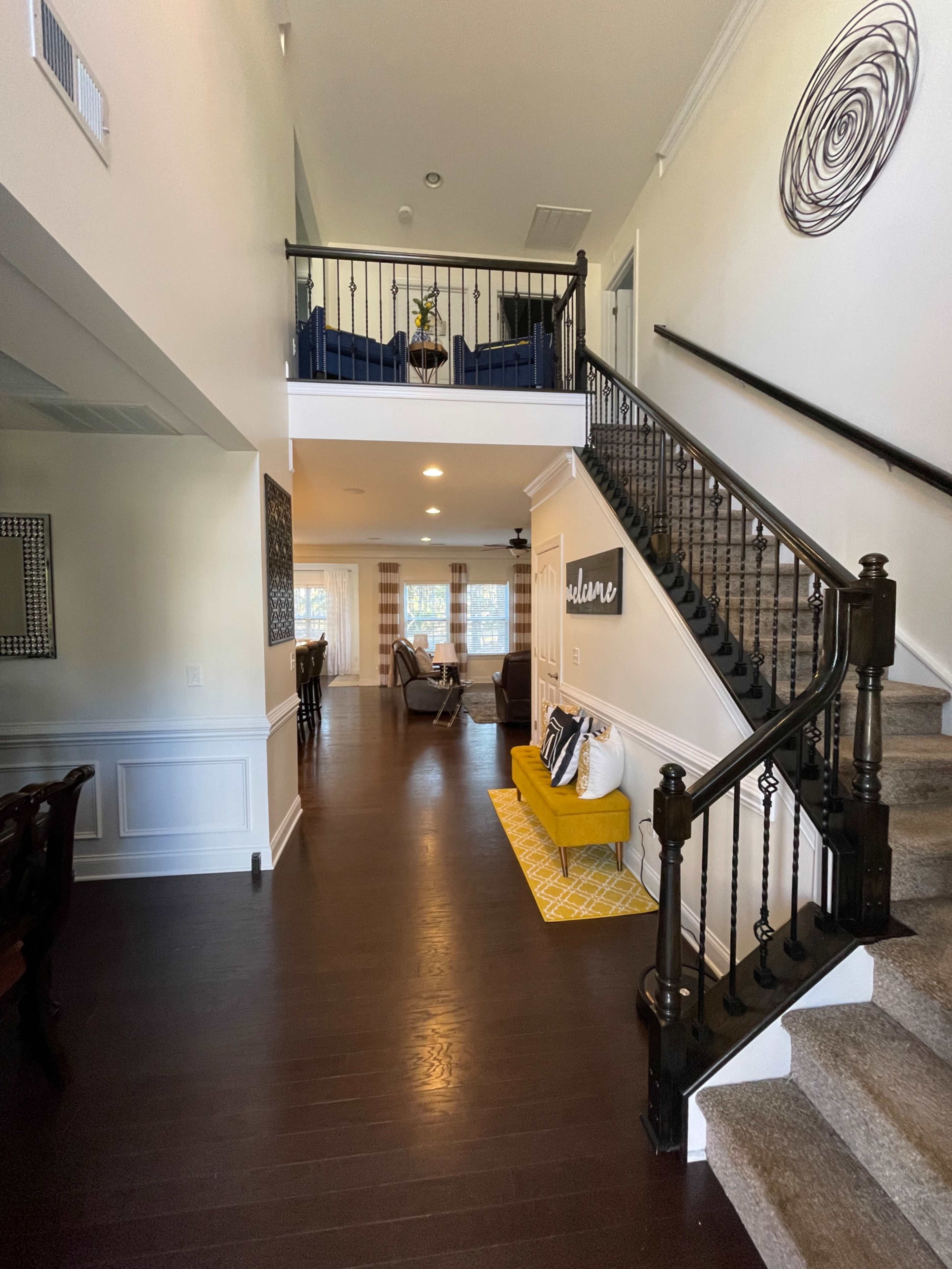 A spacious foyer with a staircase leading to an upper level, featuring a mix of hardwood and carpet flooring, and furniture arranged in the living and dining areas.