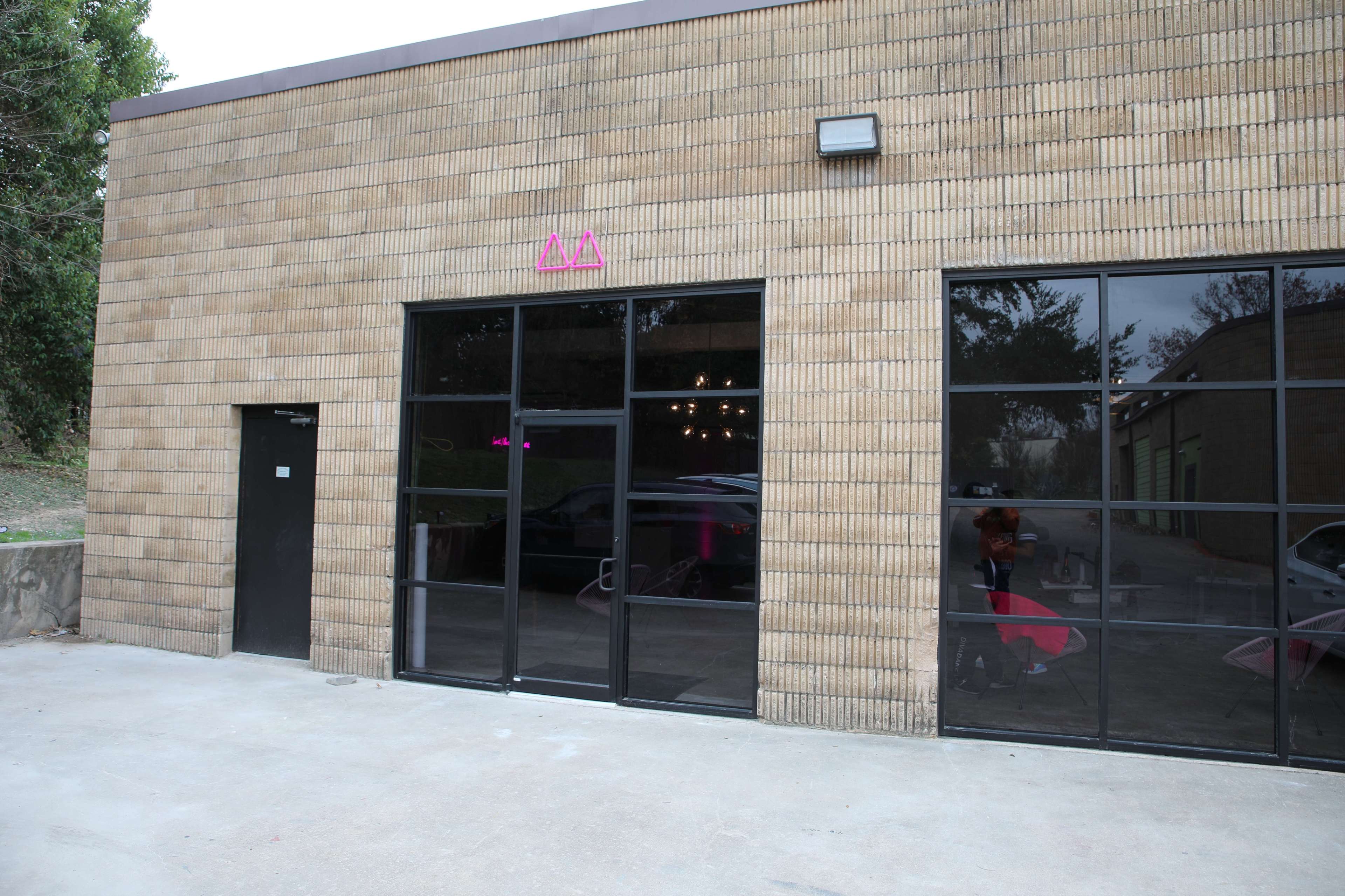 A rectangular building with a brick exterior, featuring large glass windows and a black door on the left side.