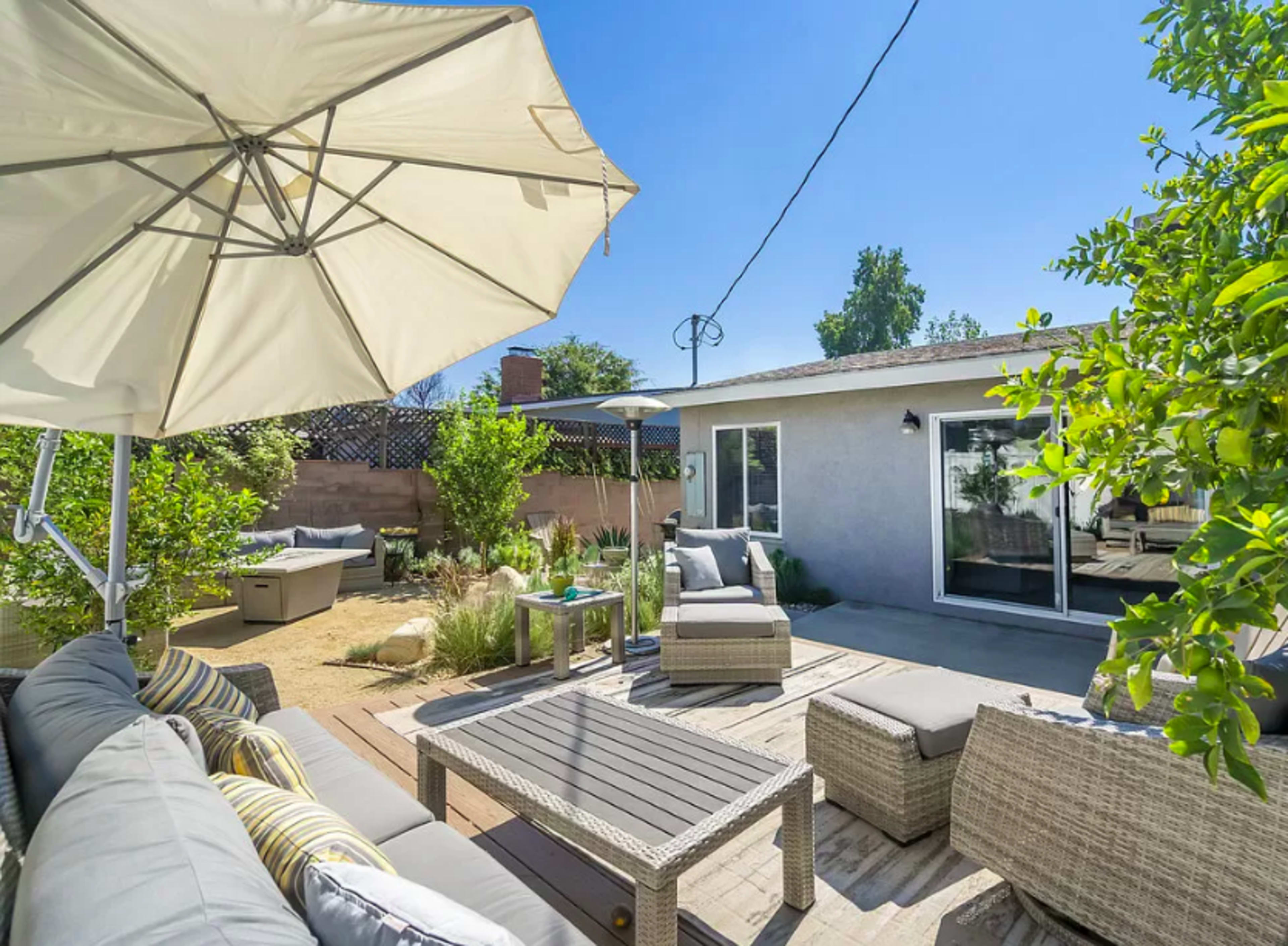 A backyard patio with a gray sofa set, a coffee table, and an umbrella next to a house.