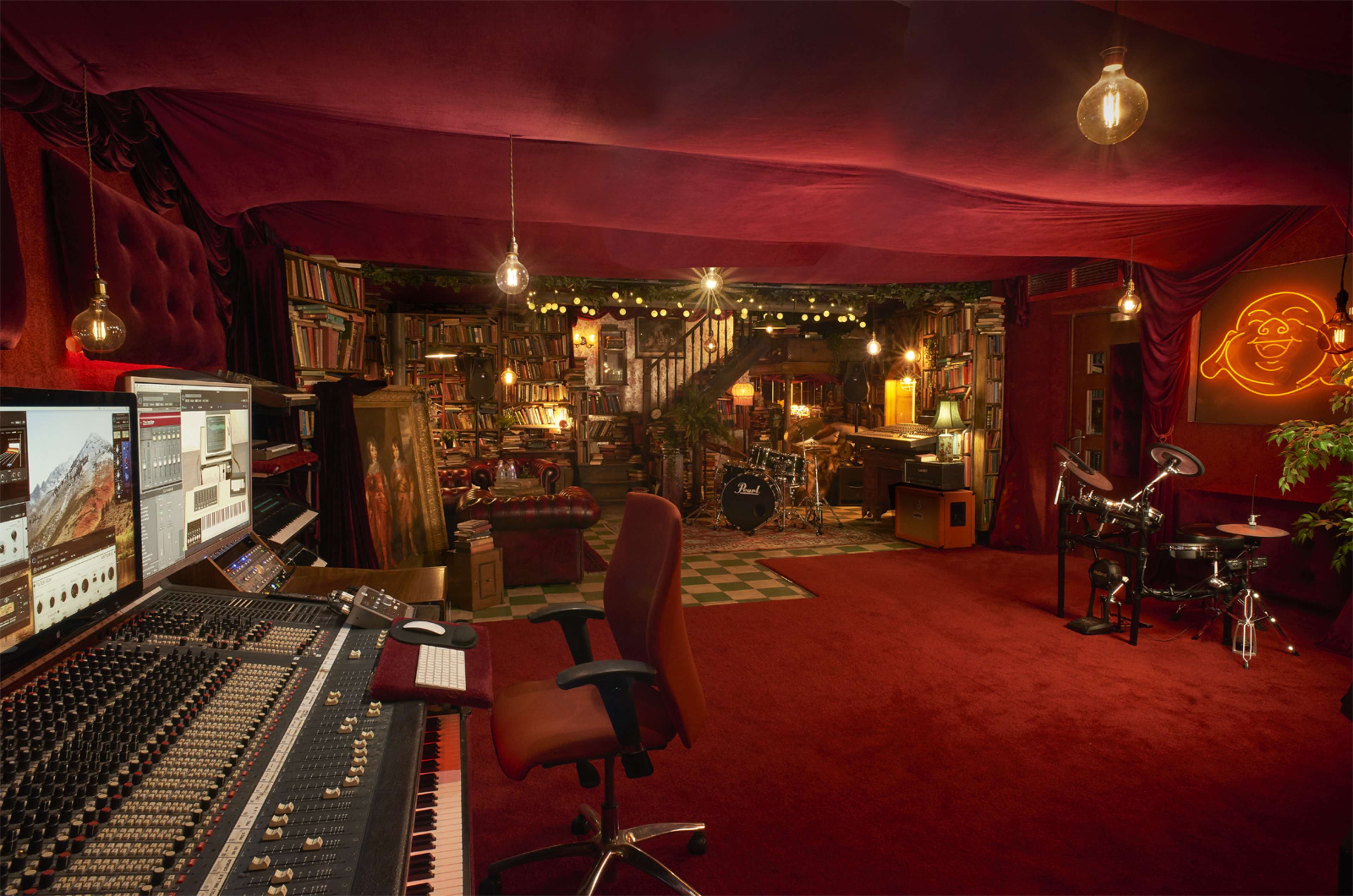 The image shows a cozy music studio filled with bookshelves, musical instruments, and warm lighting, featuring a mixing console and a chair in the foreground.