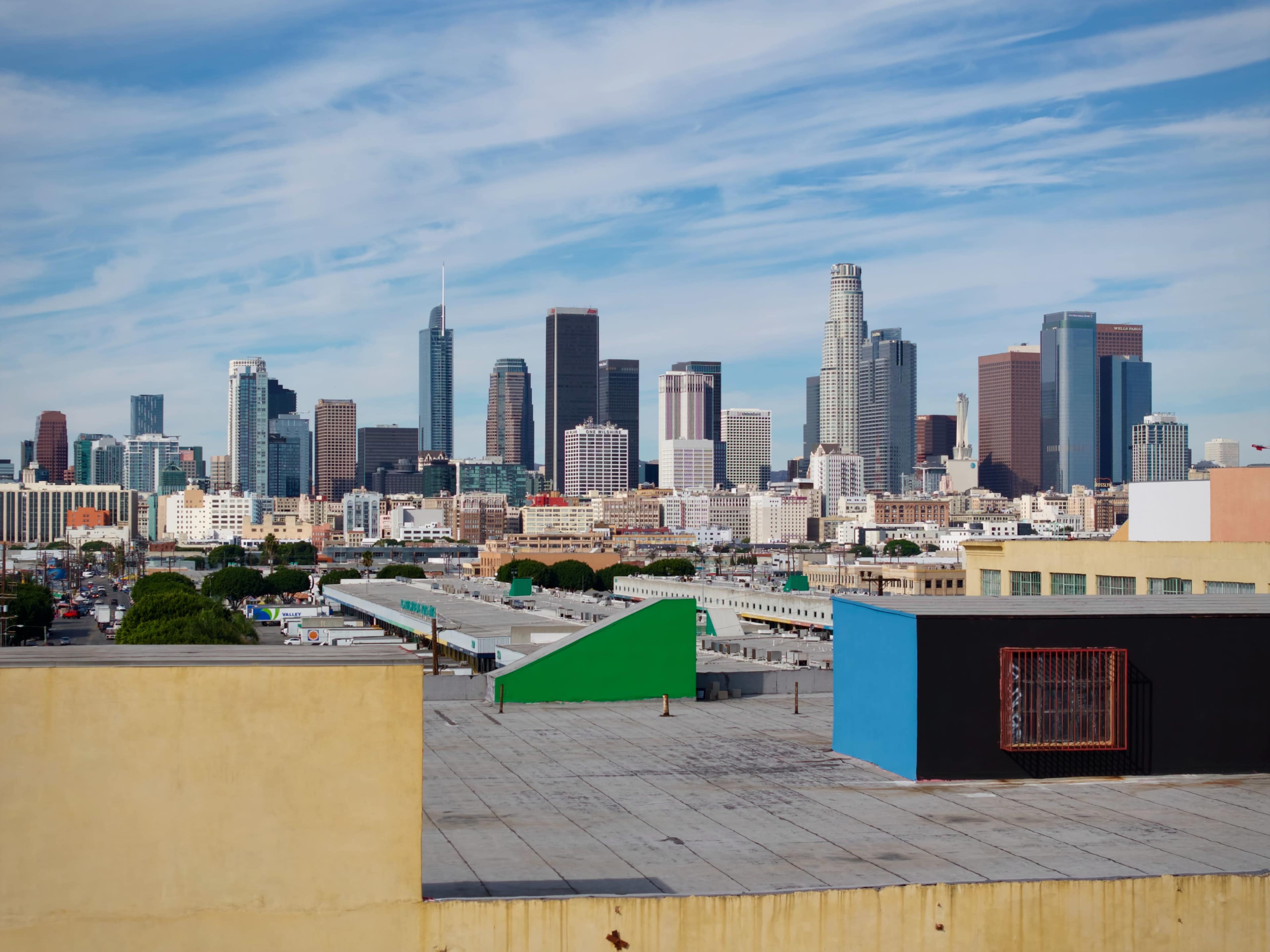 A skyline view of downtown Los Angeles features modern skyscrapers against a blue sky with clouds.