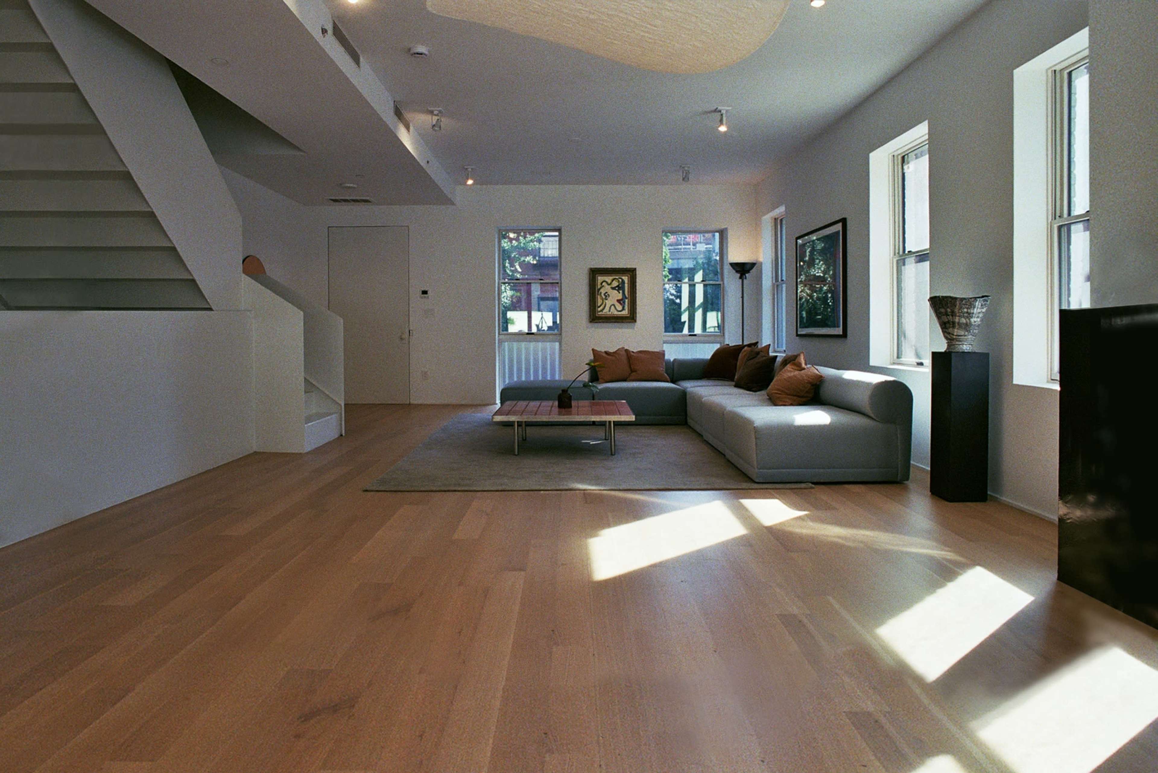 The image shows a spacious living room with a light-colored sofa, a coffee table, and large windows allowing natural light to enter.