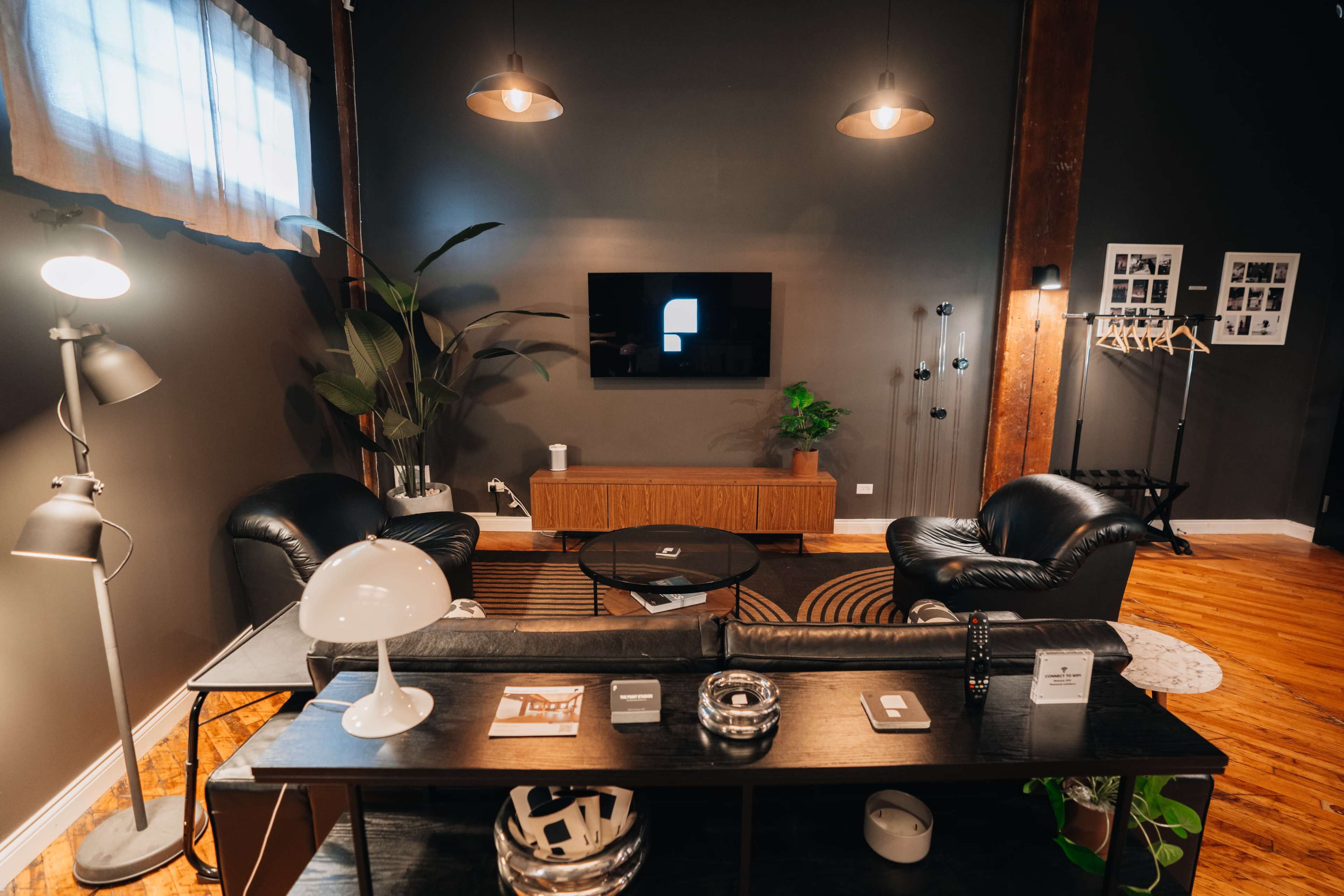 The image shows a modern living room with black leather furniture, a wooden media console, and a large television mounted on the wall.
