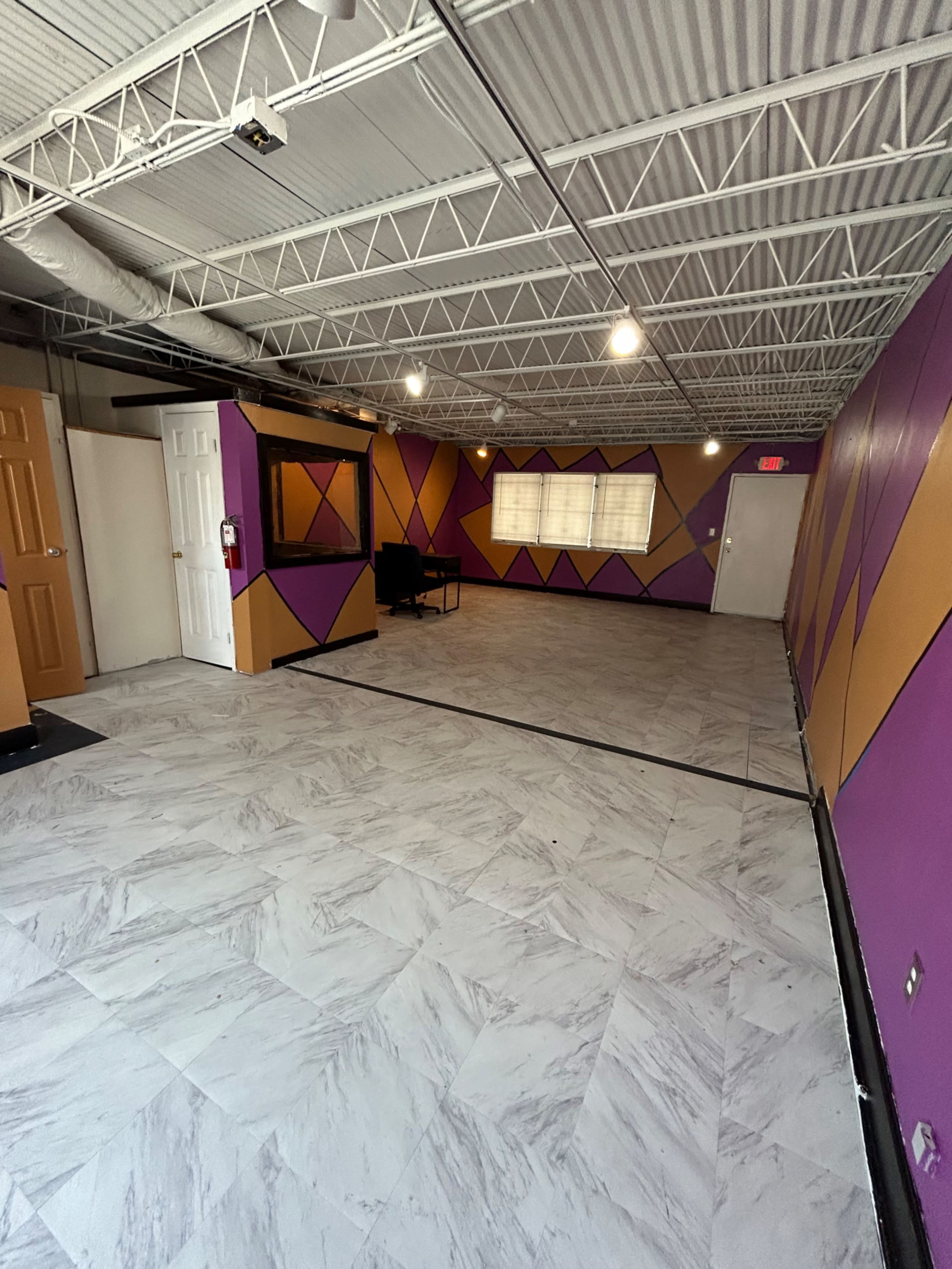 An empty room with patterned purple and orange walls, a tiled floor, and a couple of doors on one side.