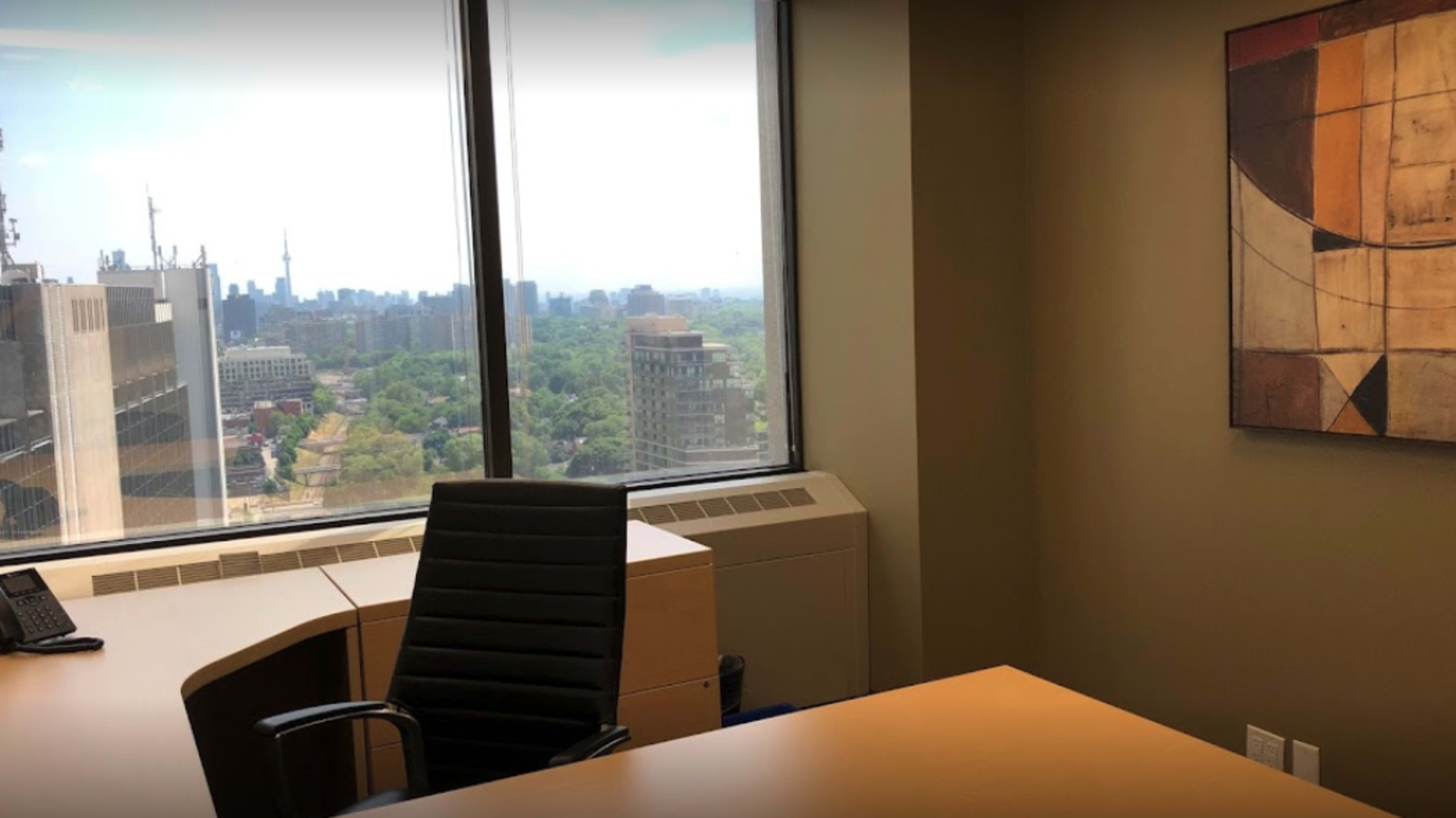 The image shows an office interior featuring a desk and chair, with large windows offering a view of a city skyline.