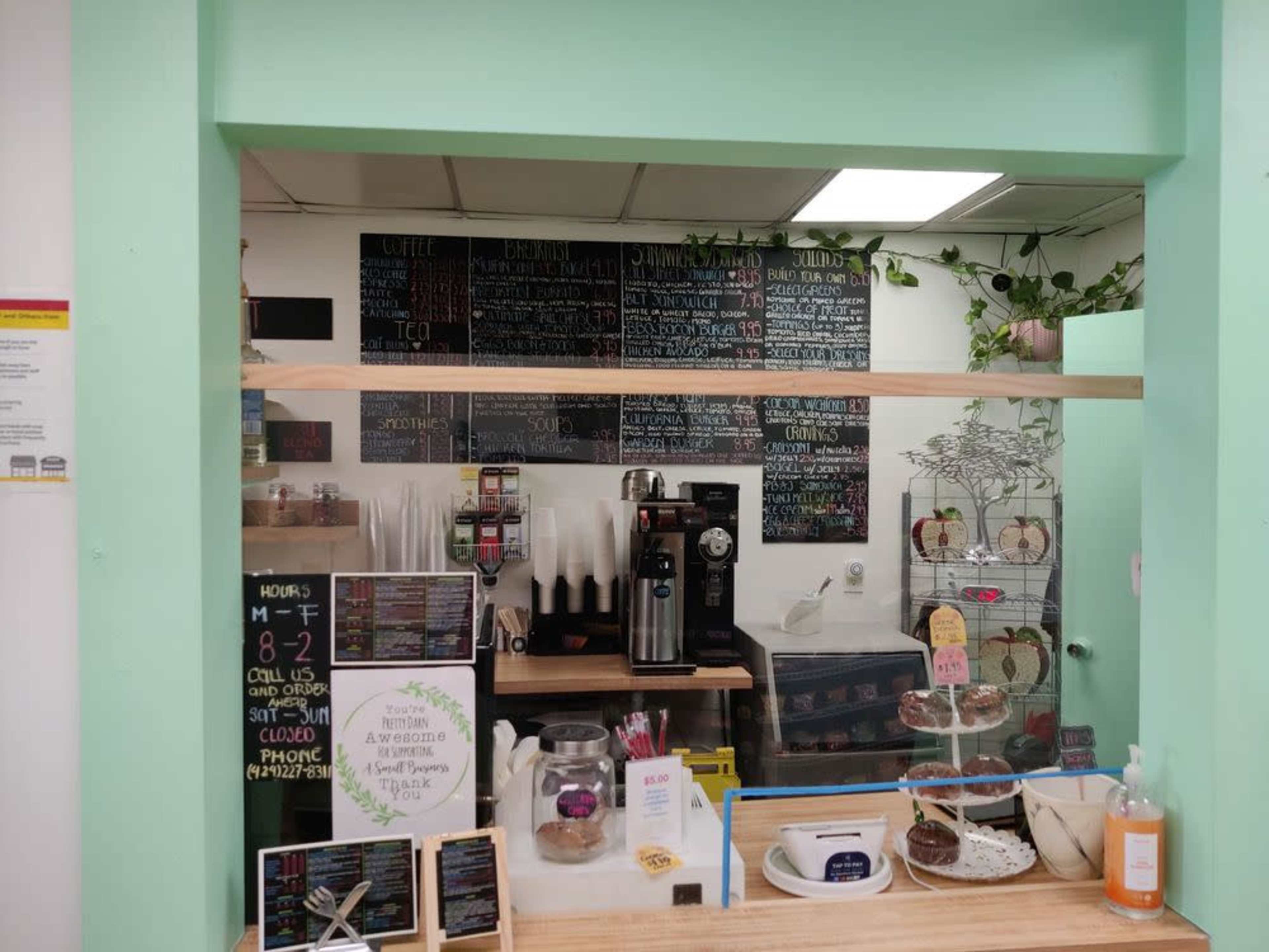 The image shows the interior of a coffee shop with a counter featuring a menu board on the wall, a coffee machine, and various baked goods displayed on the counter.
