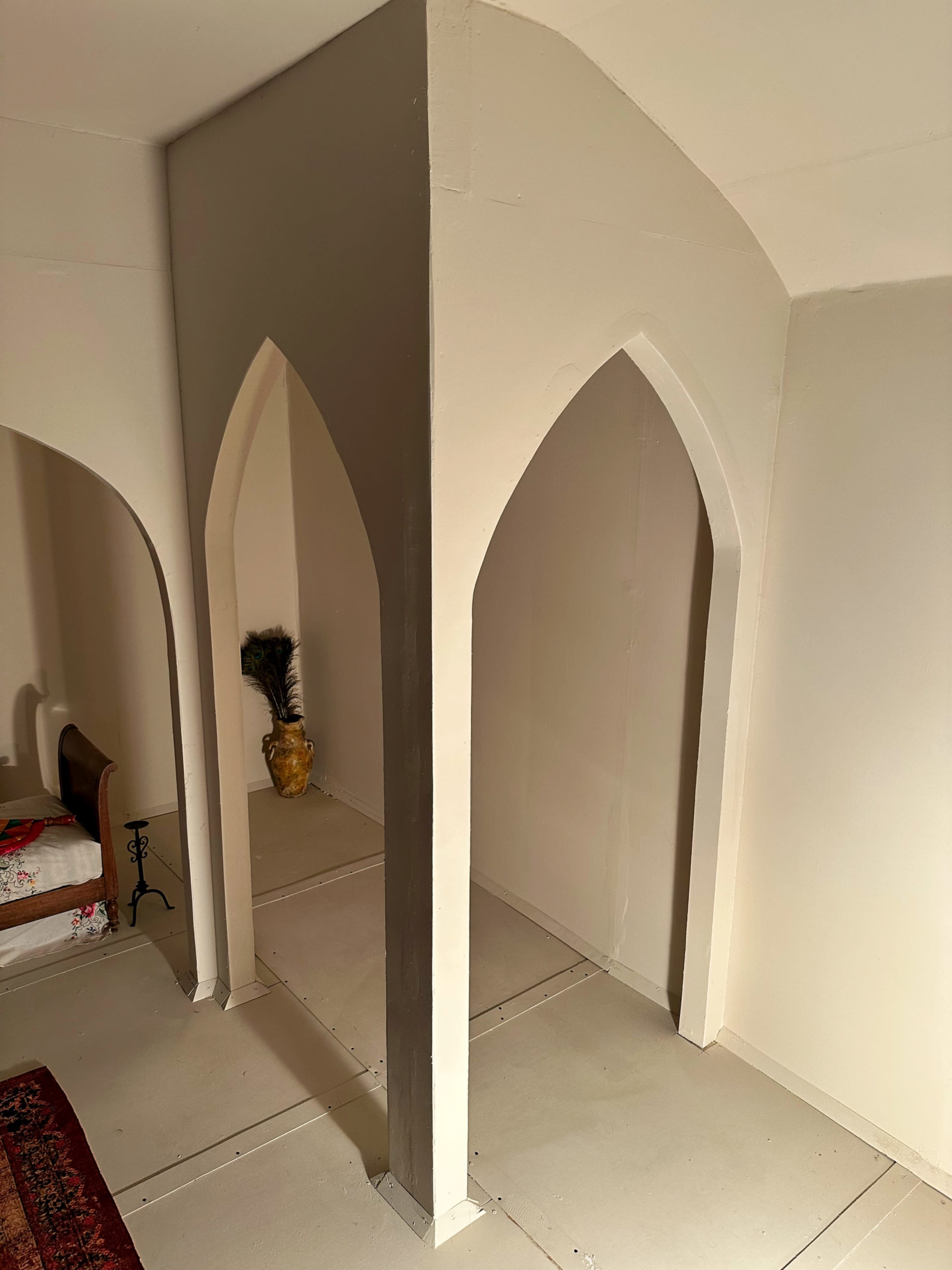 The image shows a room with white walls featuring two archways and a decorative vase in the corner.