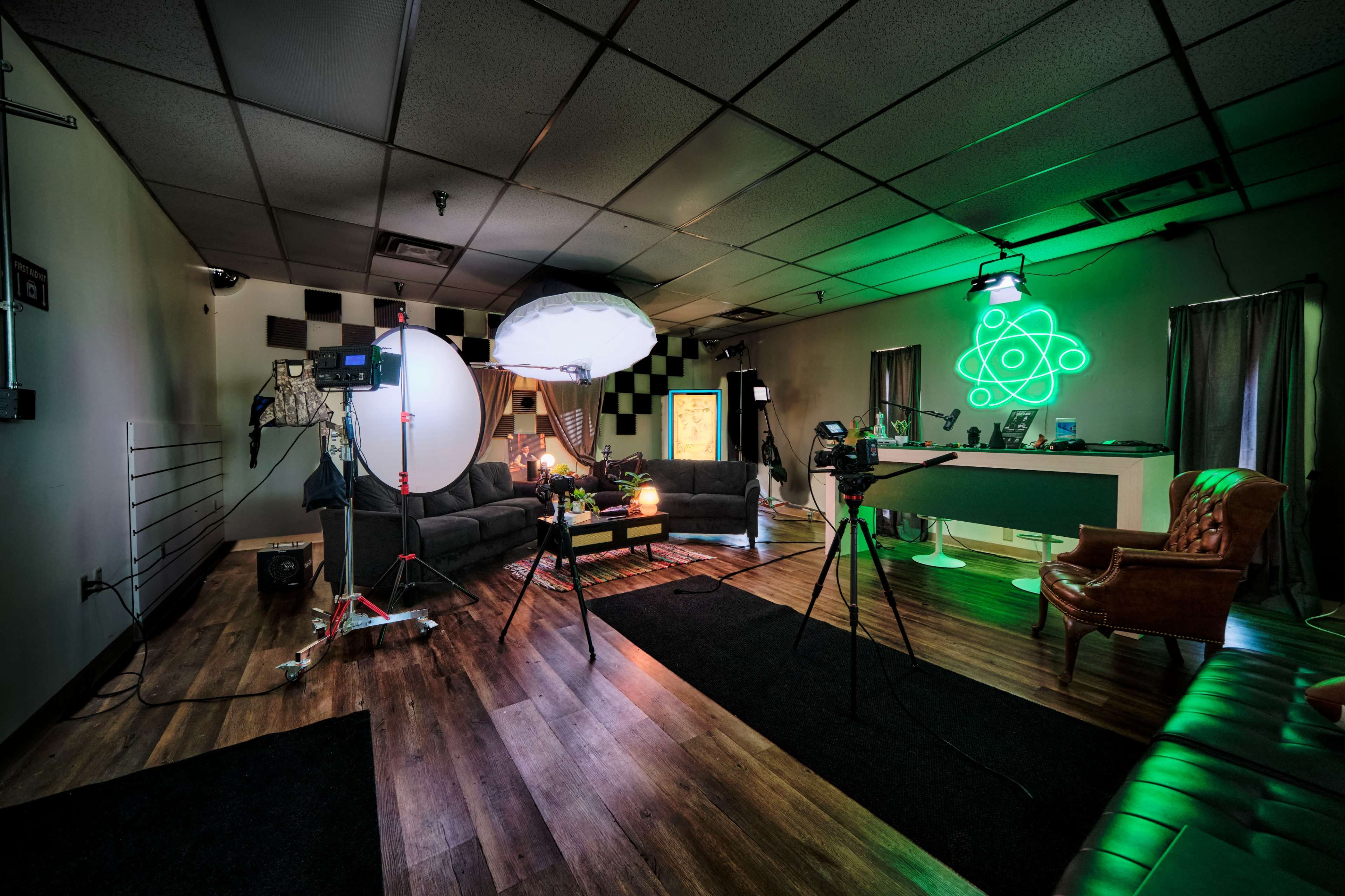A studio setup with cameras, lighting equipment, and a comfortable seating area featuring black and green decor.
